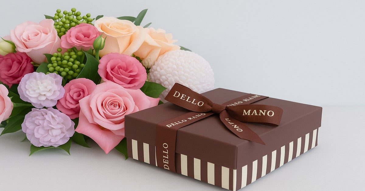 Luxury Dello Mano brownie gift box with striped base and branded ribbon, paired with an abundant bouquet of pink and peach roses, lisianthus, and seasonal flowers — a thoughtful gift combination of brownies and flowers