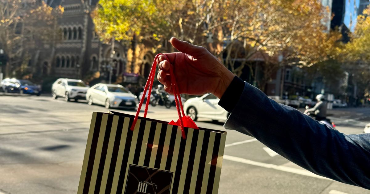 “Hand holding a Dello Mano brownie gift bag on Collins Street Melbourne, symbolising the best brownie delivery Melbourne for corporate and personal gifts