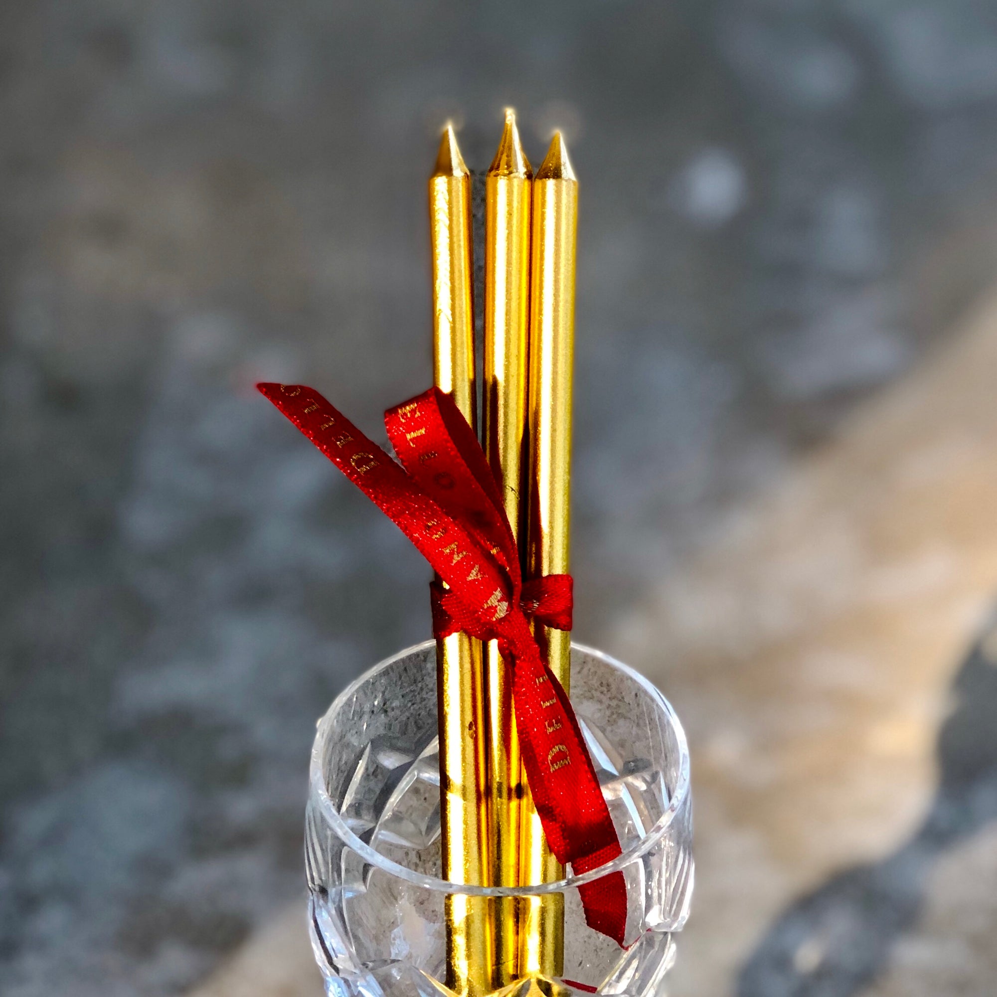 Dello Mano's signature gold candles resting on a red ribbon