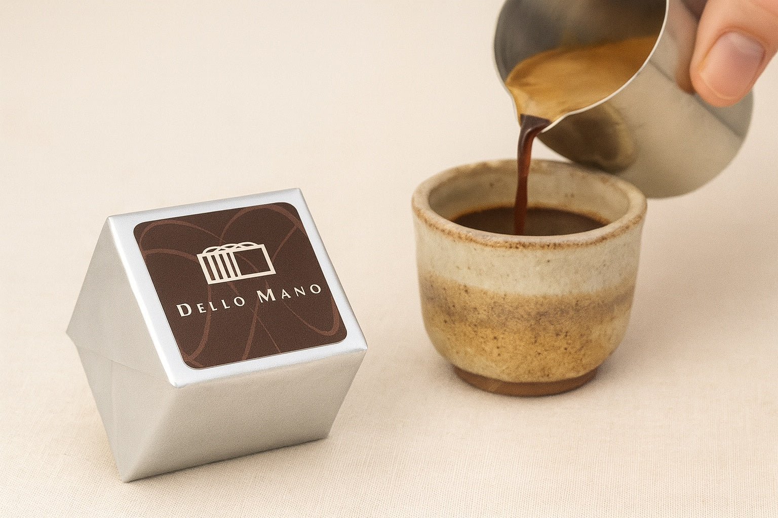 Espresso Walnut Brownie Cube by Dello Mano, wrapped in silver foil with branded label, placed beside a handmade ceramic cup as espresso is gently poured