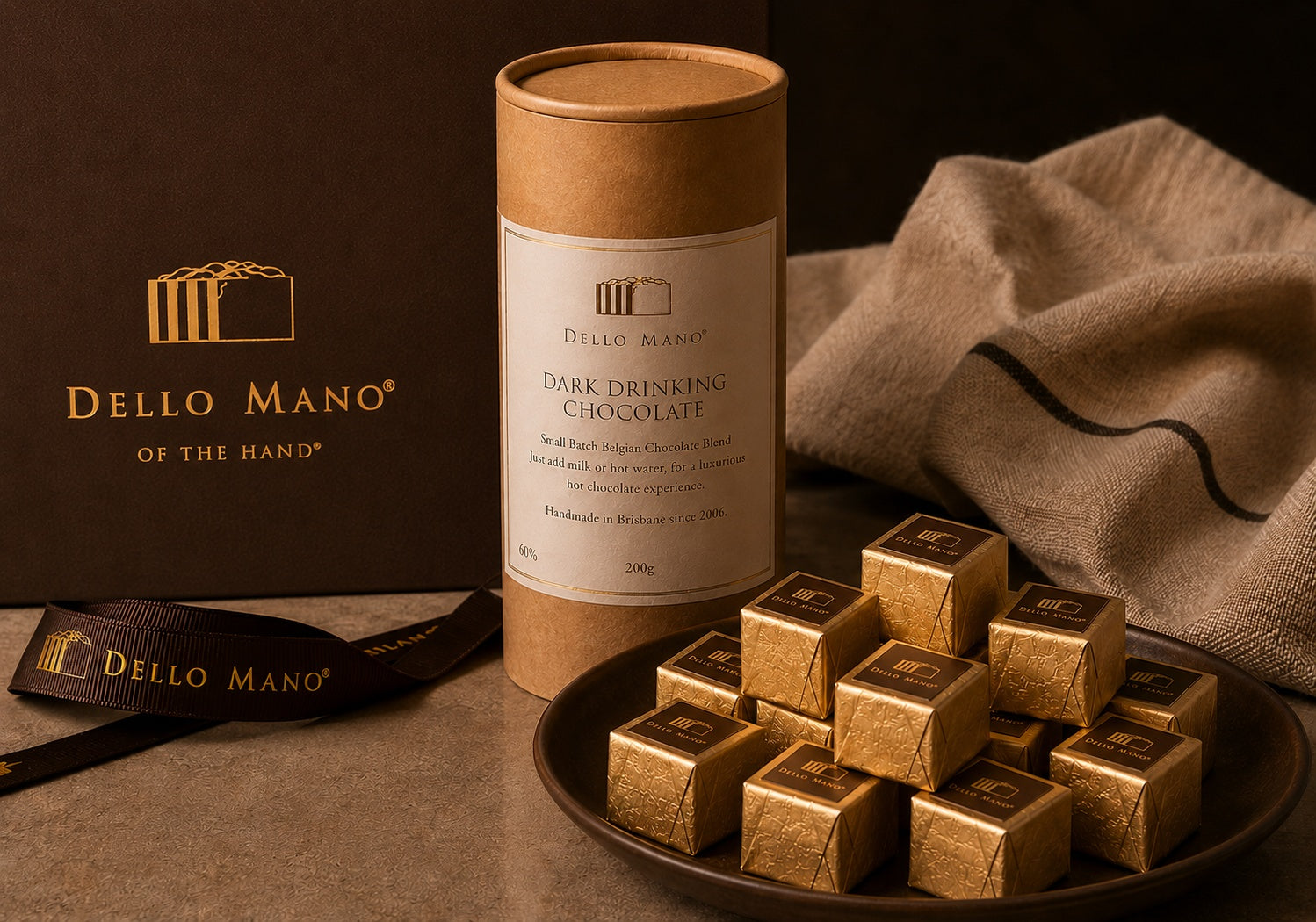 Dello Mano Dark Drinking Chocolate with gold-foiled handmade brownie cubes on a ceramic plate, celebrating our handmade chocolate heritage since 2006.