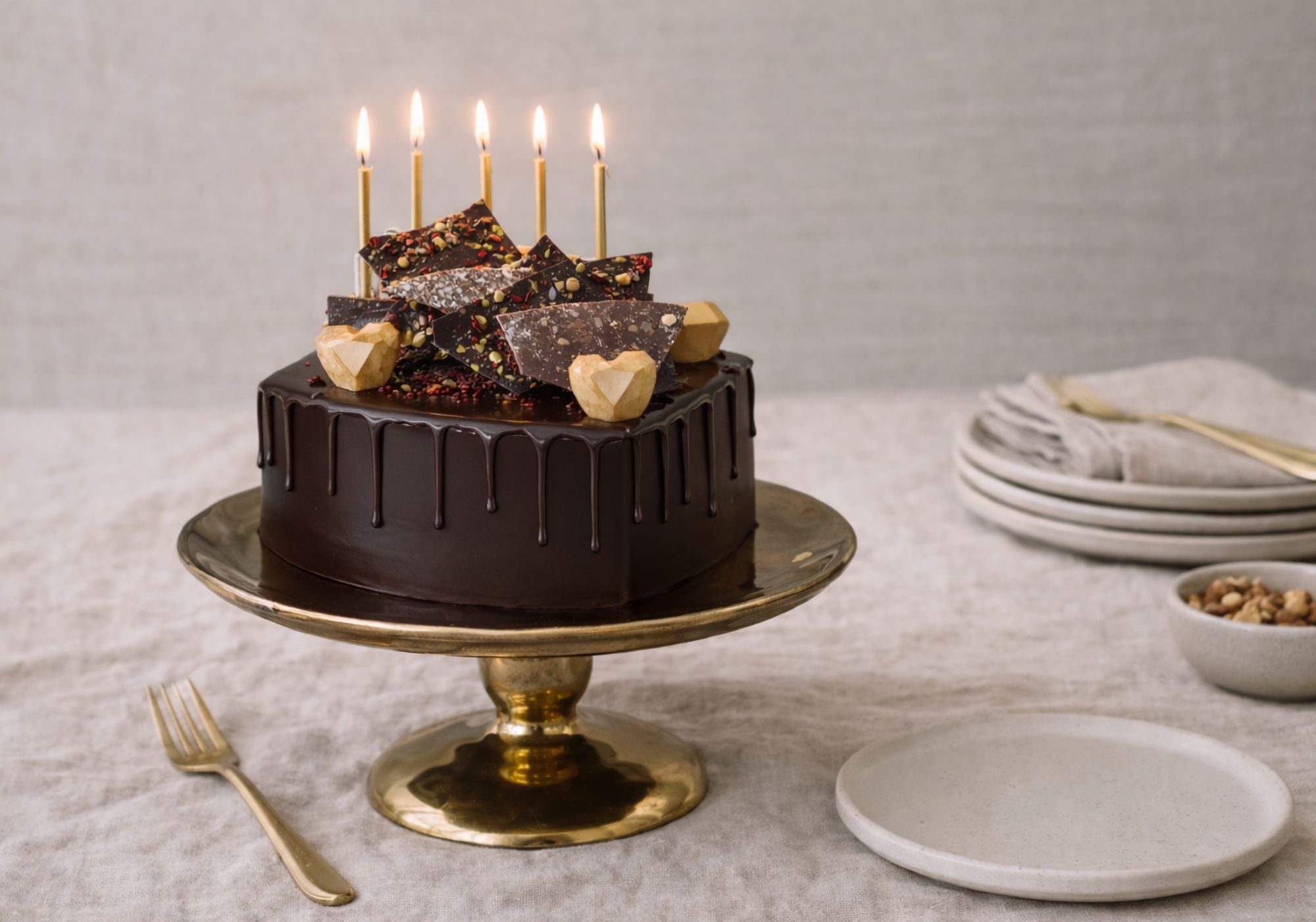 Chocolate celebration cake with glossy ganache on linen table setting with candles and plates, ready for birthday celebration.