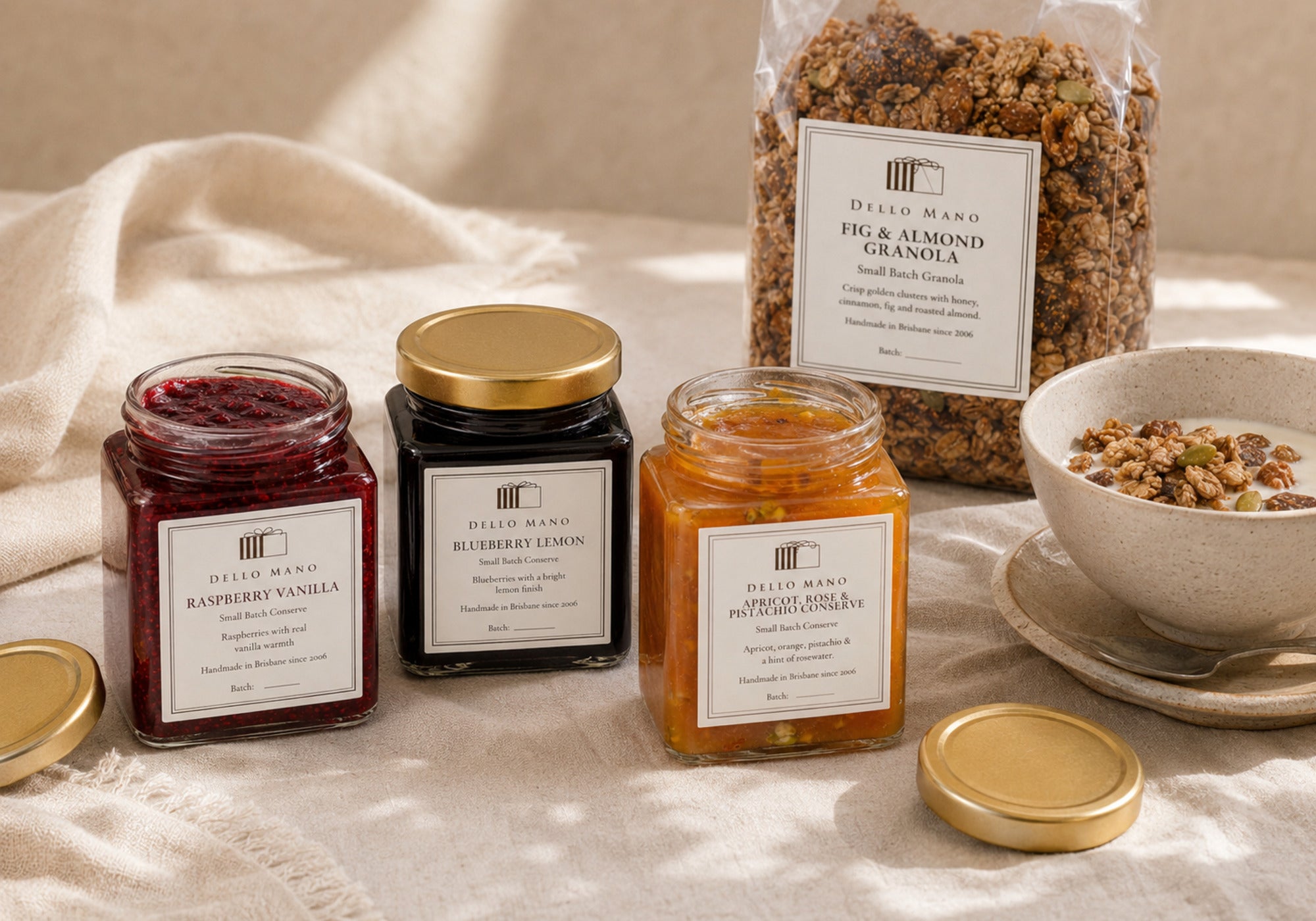 Three Dello Mano fruit preserves with Fig & Almond Granola arranged on a calm breakfast table