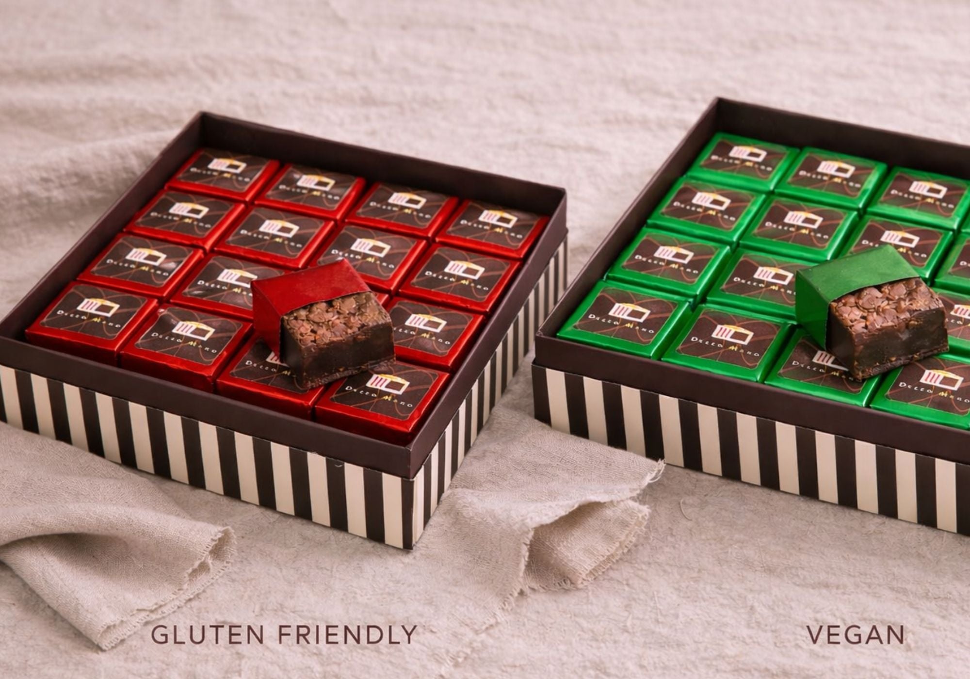 Dello Mano gluten-friendly brownie gift box and vegan brownie gift box side by side on natural linen background, handmade chocolate brownies wrapped in red and green foil.