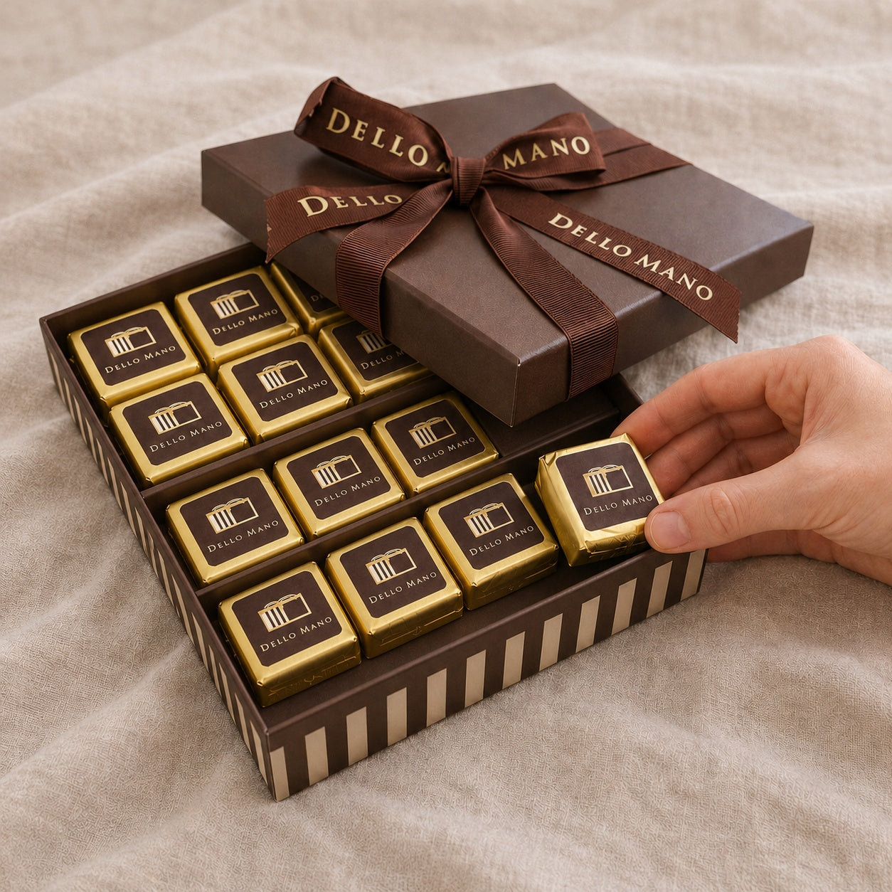 Dello Mano chocolate brownie gift box with individually wrapped brownie cubes, signature ribbon and a hand selecting one piece.