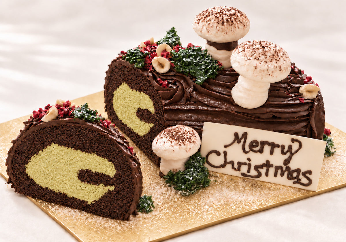 Concept image of a cut Belgian chocolate brownie Christmas log showing its pistachio cream centre, chocolate ganache, meringue mushrooms and handmade Merry Christmas plaque.