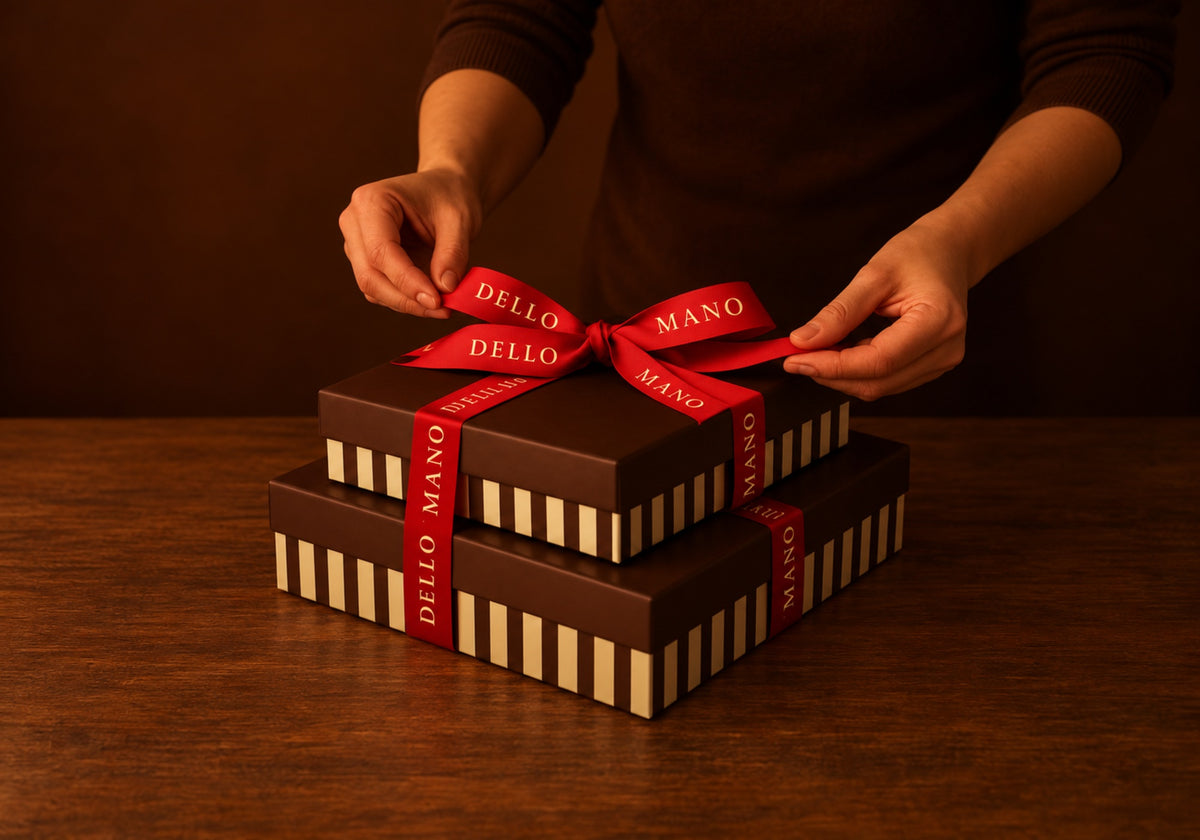 Hands tying a red Dello Mano ribbon around stacked Christmas brownie gift boxes.