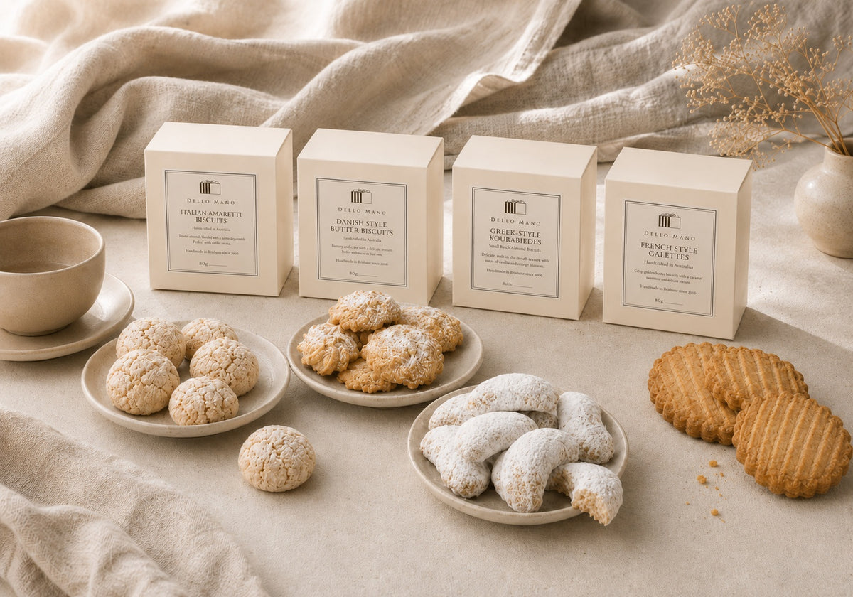 Dello Mano European Biscuit Collection with Italian Amaretti, Danish-style butter biscuits, Greek-style Kourabiedes and French-style Galettes arranged in a soft neutral lifestyle setting.