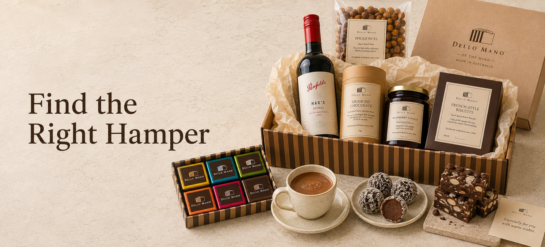Dello Mano hamper collection with wine, drinking chocolate, biscuits, preserves and colourful individually wrapped brownies on a light stone background.