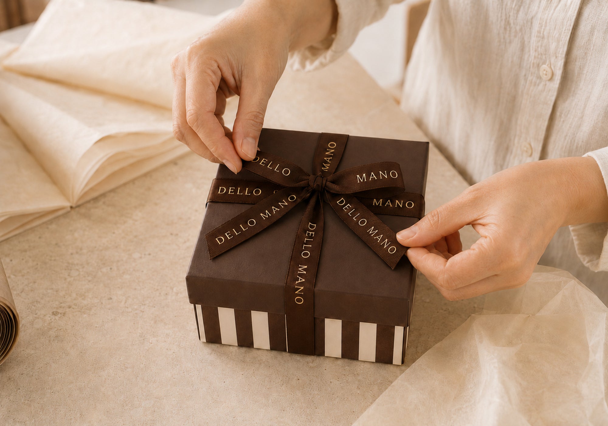 Hands carefully finishing the ribbon on a handmade Dello Mano corporate gift box.