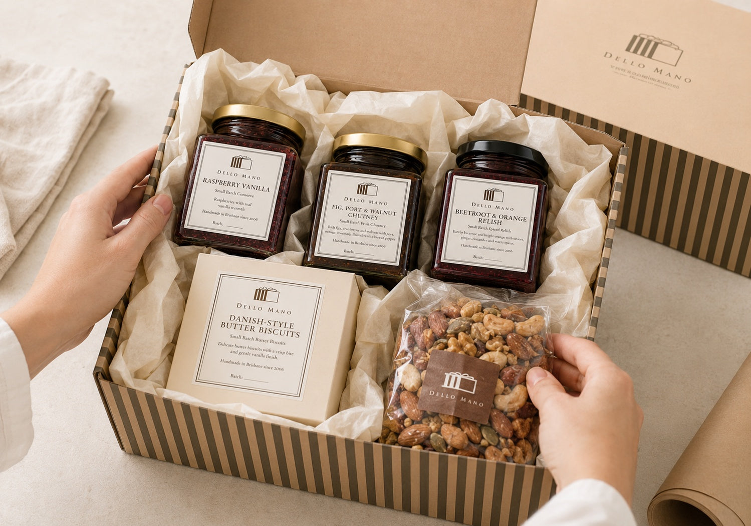 Dello Mano Sweet & Savoury Hamper being packed by hand with Raspberry Vanilla Jam, Fig Port and Walnut Chutney, Beetroot and Orange Relish, Danish-style butter biscuits and spiced nuts in cream tissue.