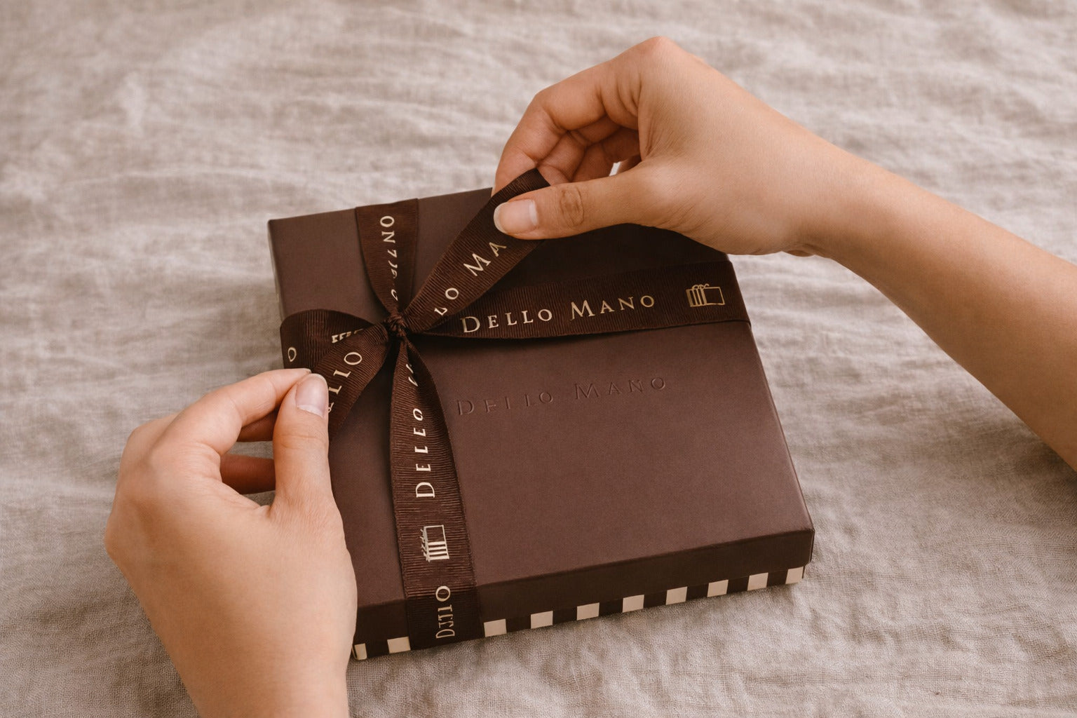 Hand tying ribbon on luxury brownie gift box showing handmade packaging process on linen background