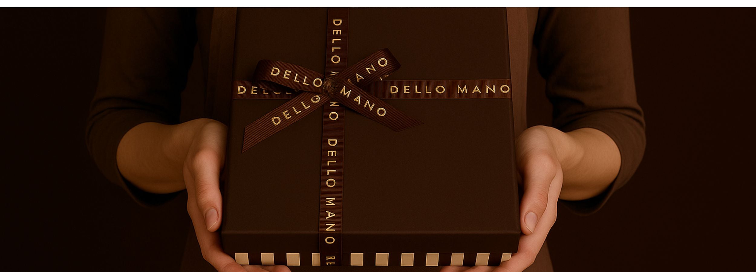 Person holding a Dello Mano Vegan Brownie gift box with 'Dello Mano' branding against a dark background