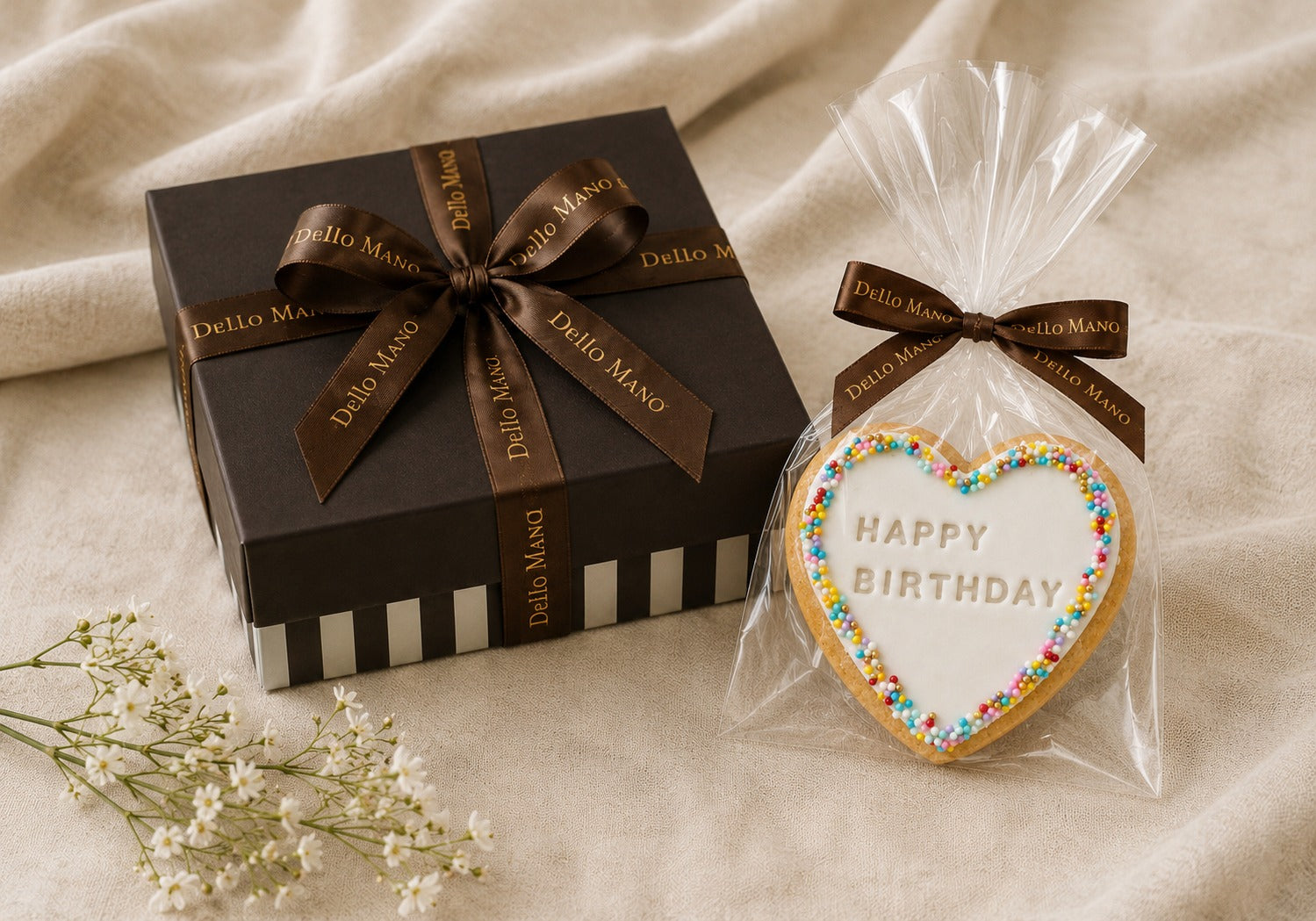 Happy Birthday Heart Cookie by Dello Mano presented as a gift add-on alongside a luxury brownie gift box, featuring a handmade vanilla butter cookie individually wrapped with ribbon on a linen background.