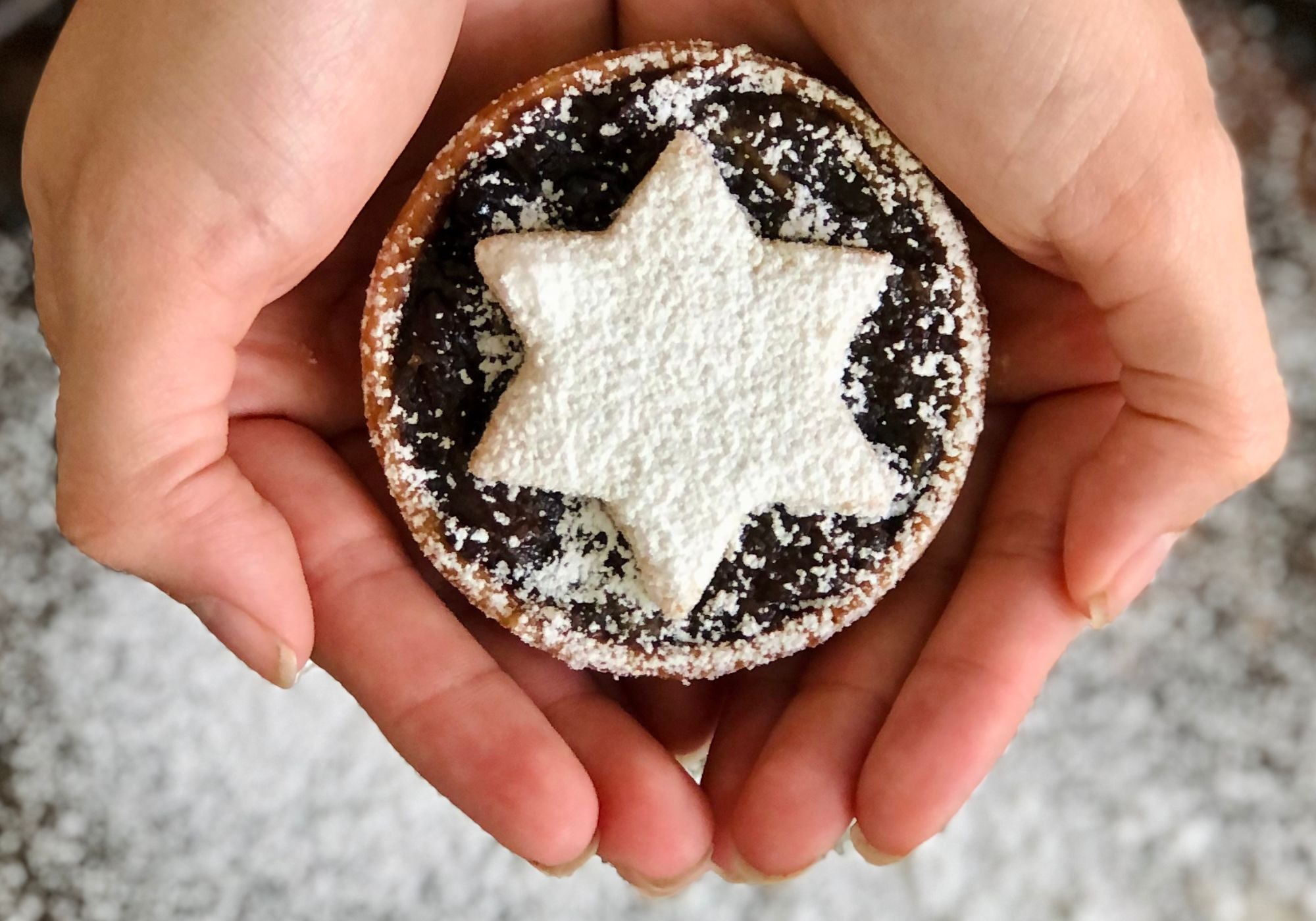 Hand holding a handmade Christmas mince pie topped with a star-shaped shortbread and dusted with icing sugar.