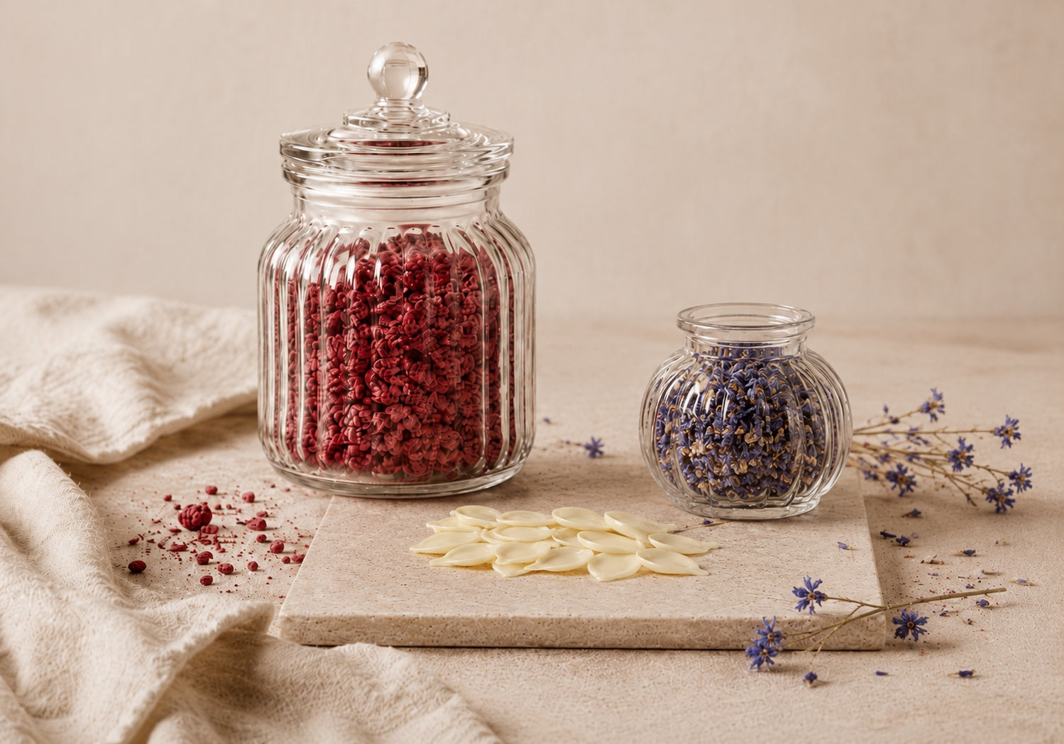 Dried raspberry crumb, dried cornflowers in a small glass jar and handmade Belgian white chocolate petals arranged on a warm neutral surface for Raspberry Blossom cake.