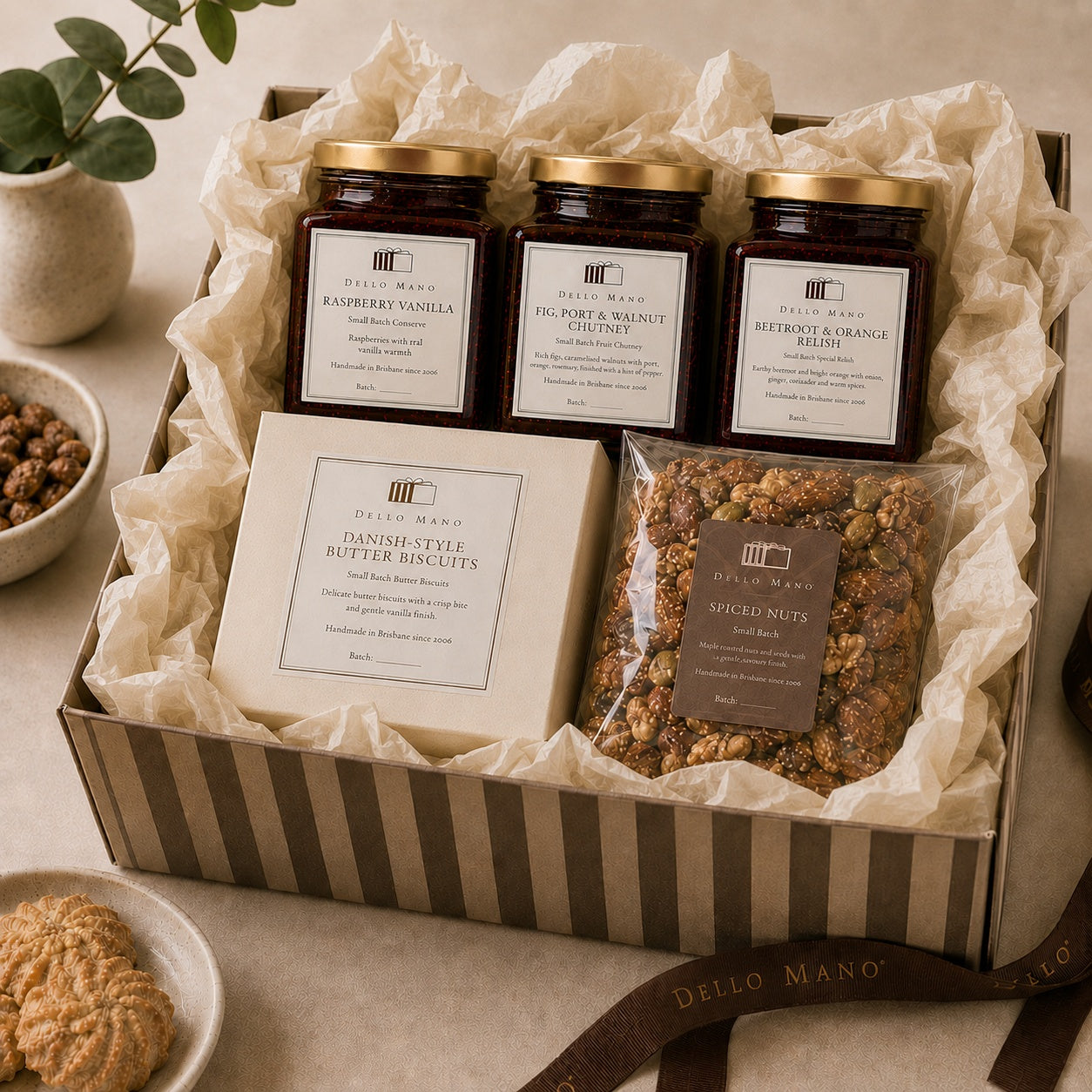 Dello Mano Sweet & Savoury Hamper with Raspberry Vanilla Jam, Fig Port and Walnut Chutney, Beetroot and Orange Relish, Danish-style butter biscuits and spiced nuts arranged in a striped gift box with cream tissue.