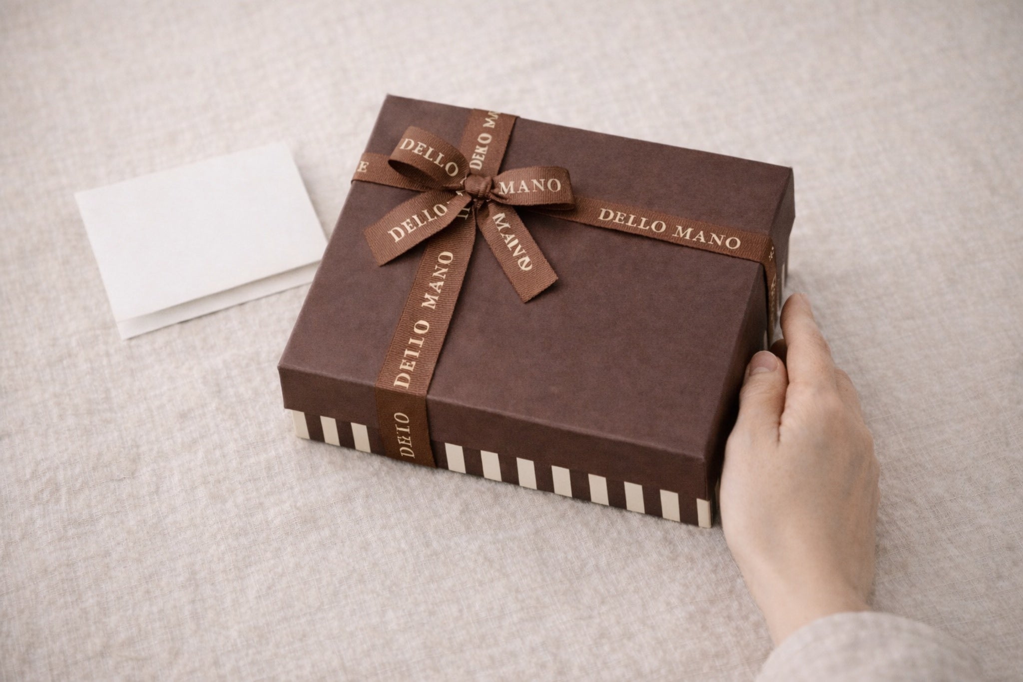 Handmade Dello Mano brownie gift box with ribbon held by hands on linen surface, styled as a thoughtful thank you gift ready for delivery across Australia