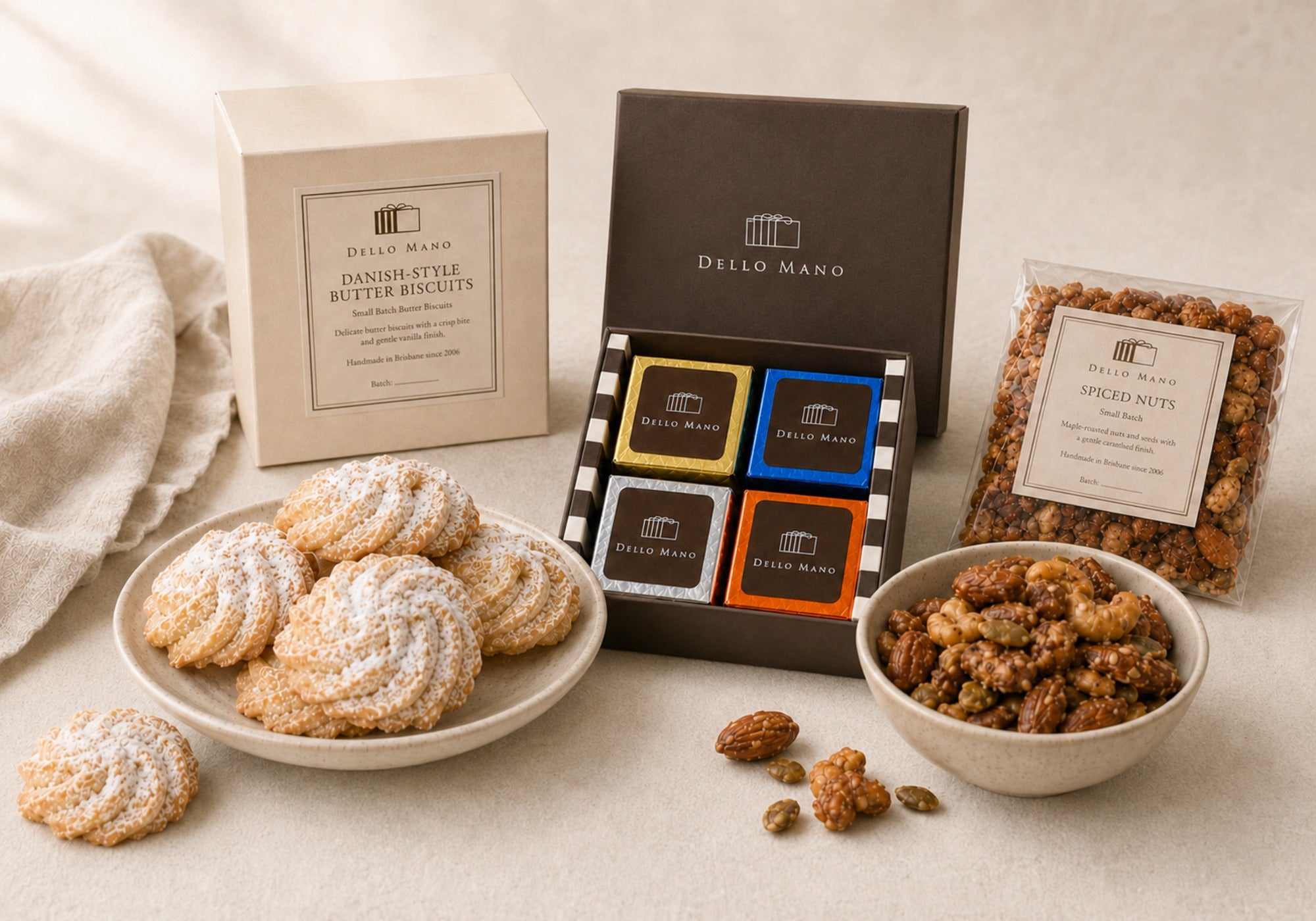 Dello Mano four-piece mixed brownie gift box, Danish Butter Biscuits and spiced nuts displayed with their packaging in a calm food-first setting.