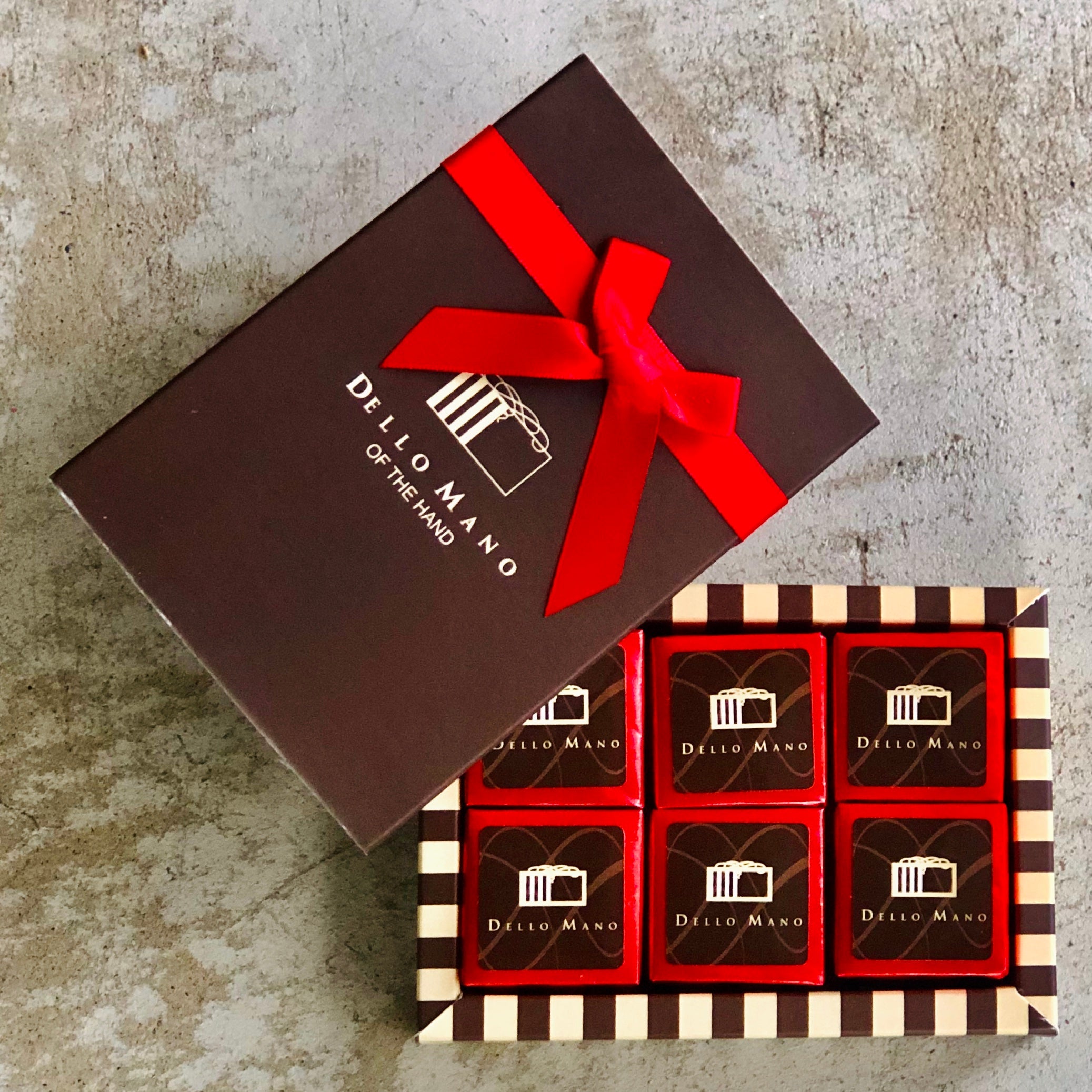 A small gift box of gluten free brownies. Each brownie is individually foiled with a brown label that says Dello Mano