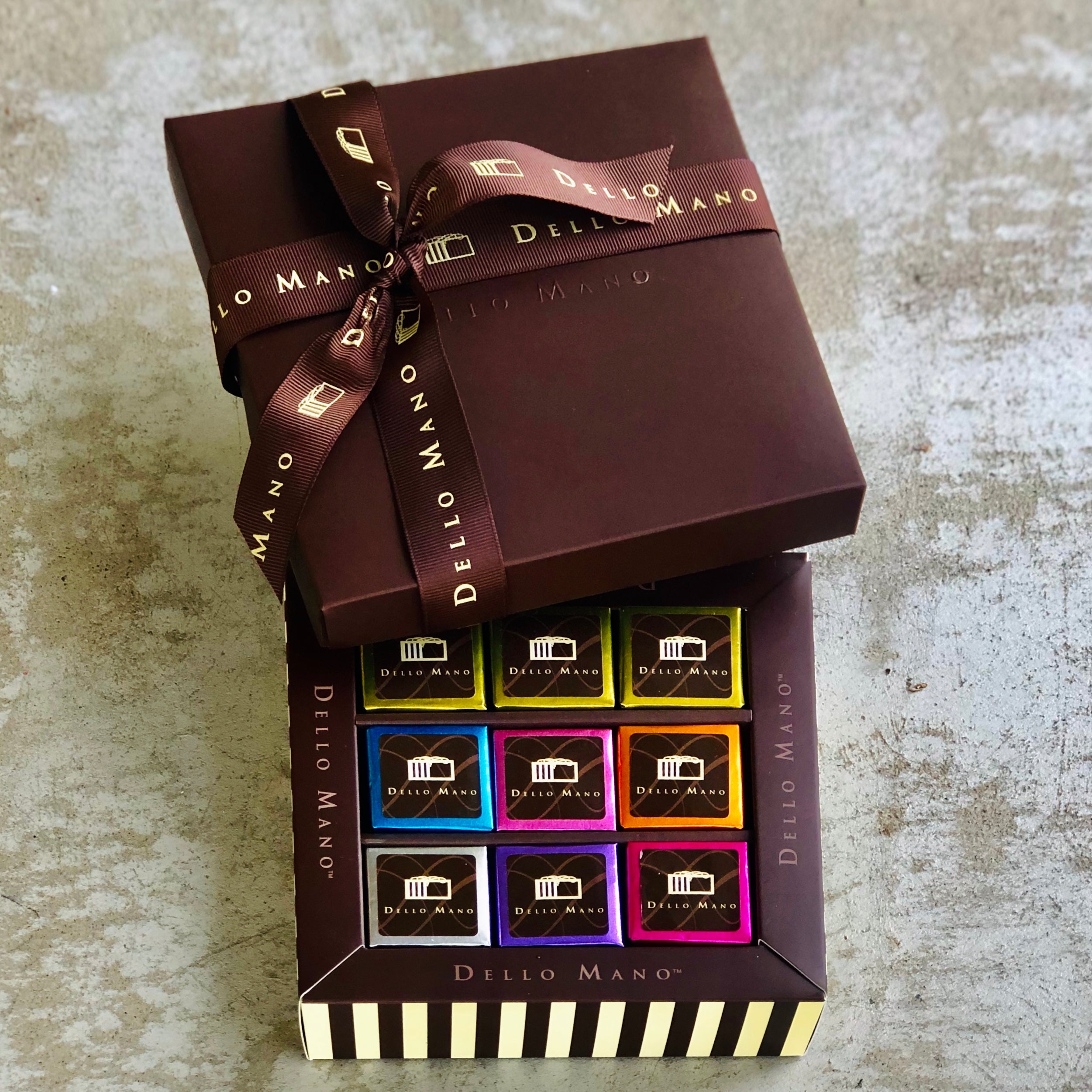 A nine piece box of mixed brownies each individually foiled. Labels each say Dello Mano and the gift box lid on top had brownie ribbon.