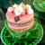 A pink cake on a green stand with Dello Mano Label