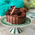 The Divine jChocolate Mousse Cake sitting on a green and white cake stand. In the background is magazine and a green pillow.