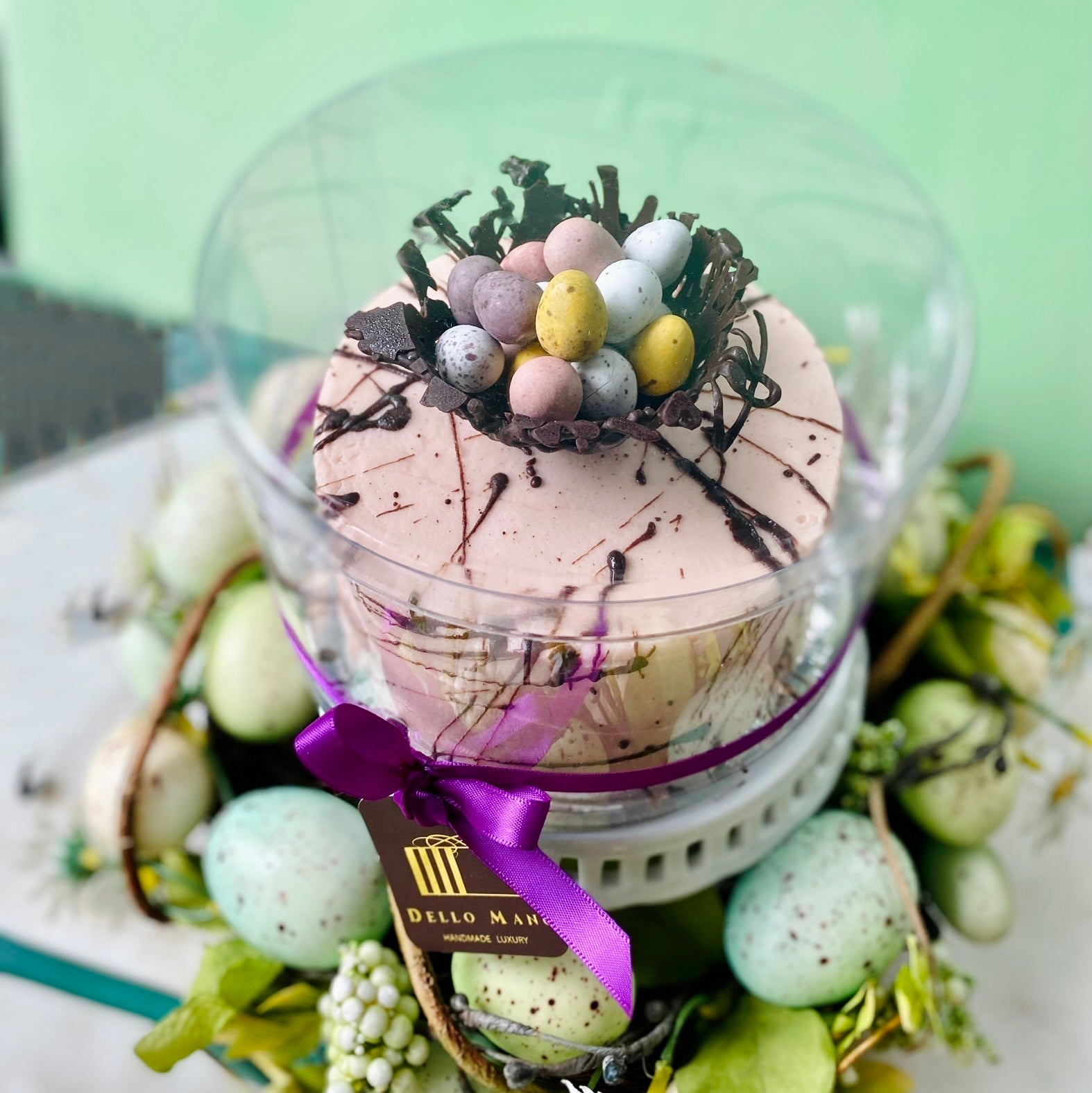 An Easter Cake with pink frosting and speckled chocolate. On top of the cake is a chocolate nest filled with Easter egg.