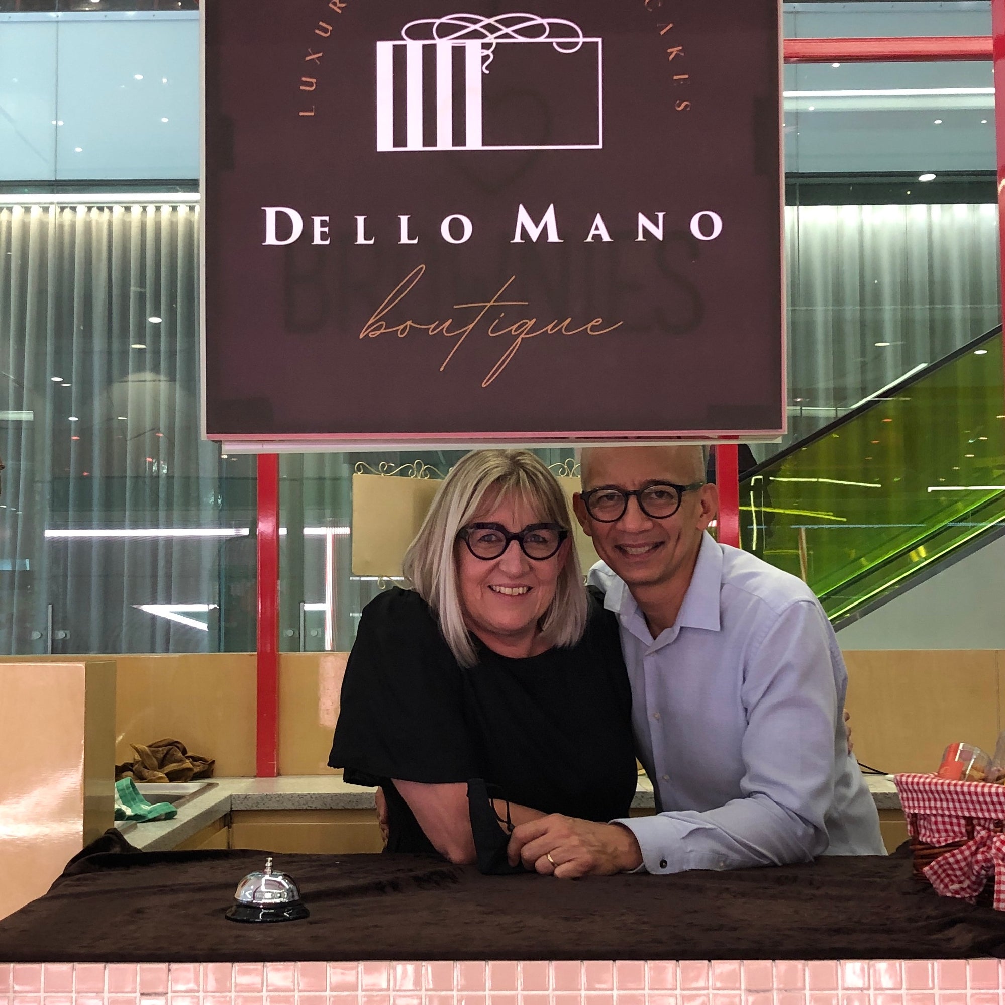 Deb and Bien Peralta owners of small business stand under the logo and sign that says Dello Mano