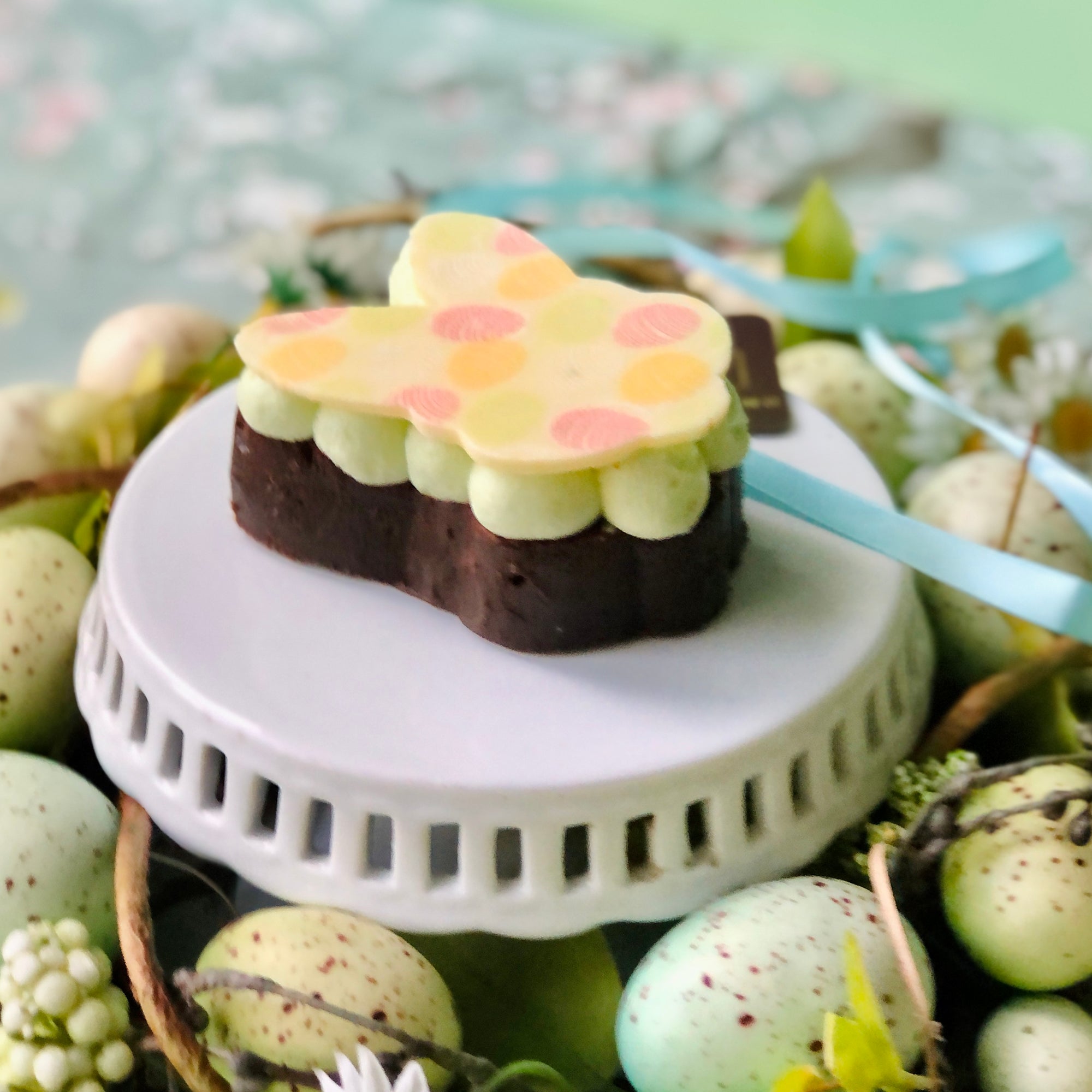 The Dello Mano Easter Bunny Brownie gift on a white stand surrounded by Easter Eggs.