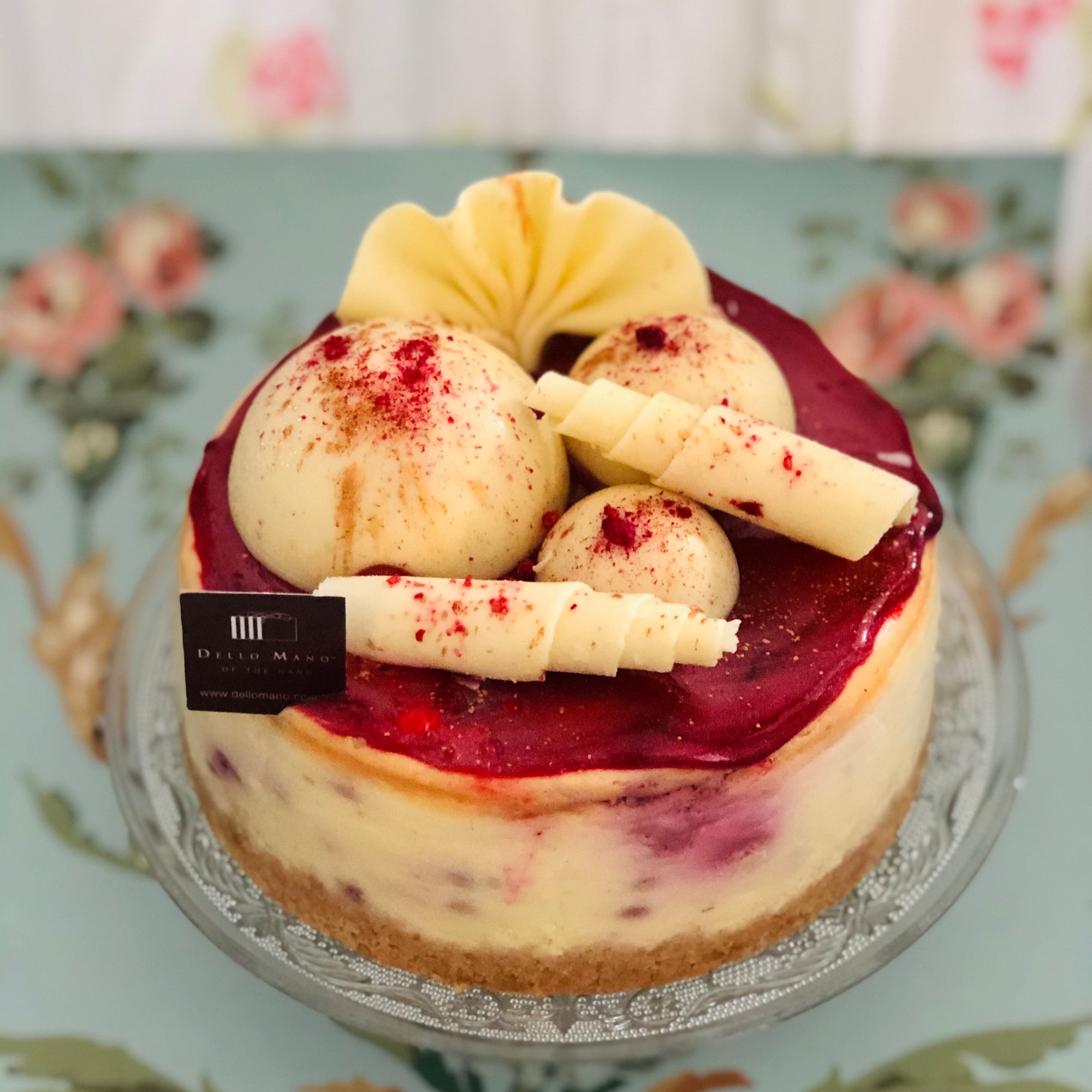 White Chocolate Raspberry Cheesecake with white chocolate decorations, and tag that says Dello Mano