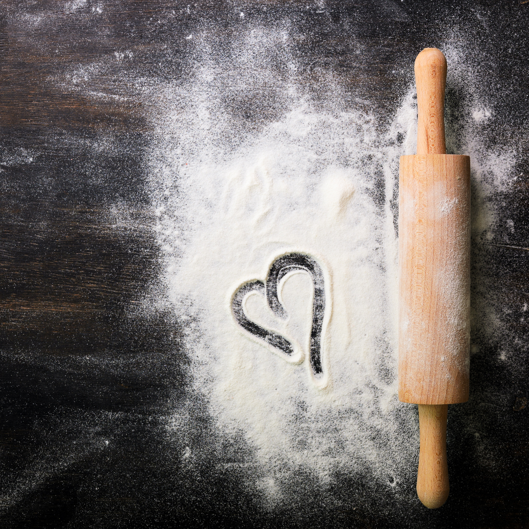A blackboard with heart written in flour and a rolling pin at the side