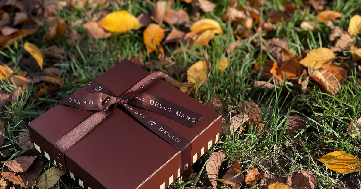 Dello Mano handmade brownie gift box tied with brown grosgrain ribbon, resting on autumn grass with golden leaves,  symbolising luxury brownie delivery across Melbourne and Victoria.