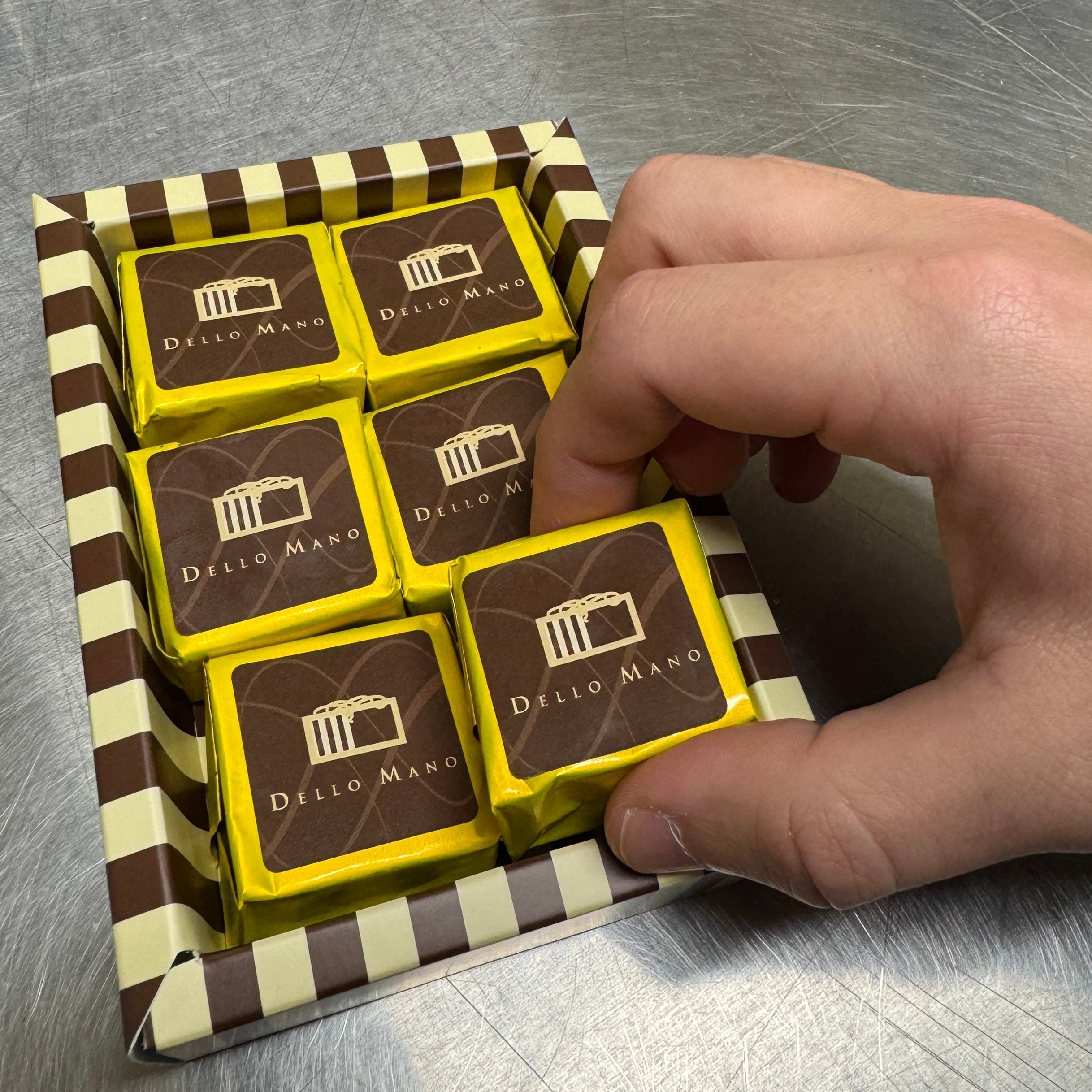 Dello Mano luxury brownies in a gift box with a hand removing one gold cube