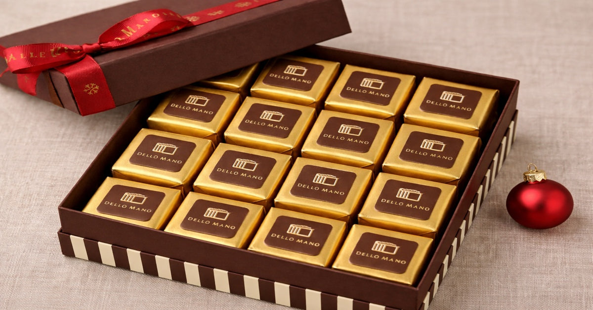 Christmas chocolate gift box Australia with gold wrapped Dello Mano brownie cubes in structured presentation and red ornament on natural linen background