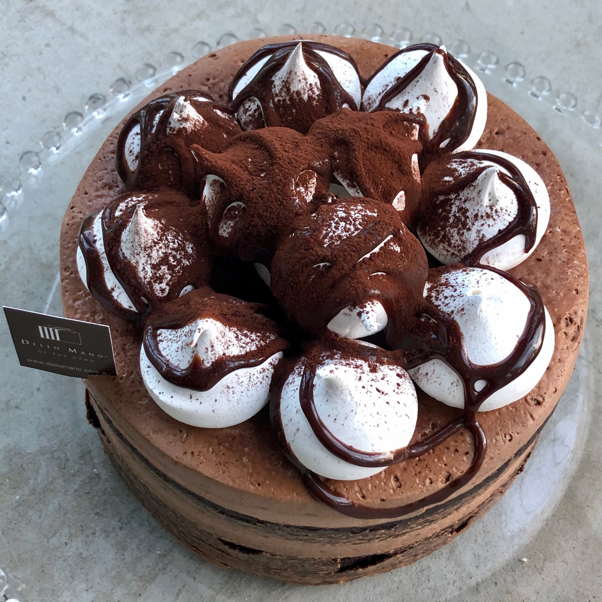 A chocolate cake with white meringues drizzled with chocolate sauce and dus