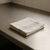 Folded white kitchen towel with grey stripes resting on a clean stainless steel bench in a commercial kitchen