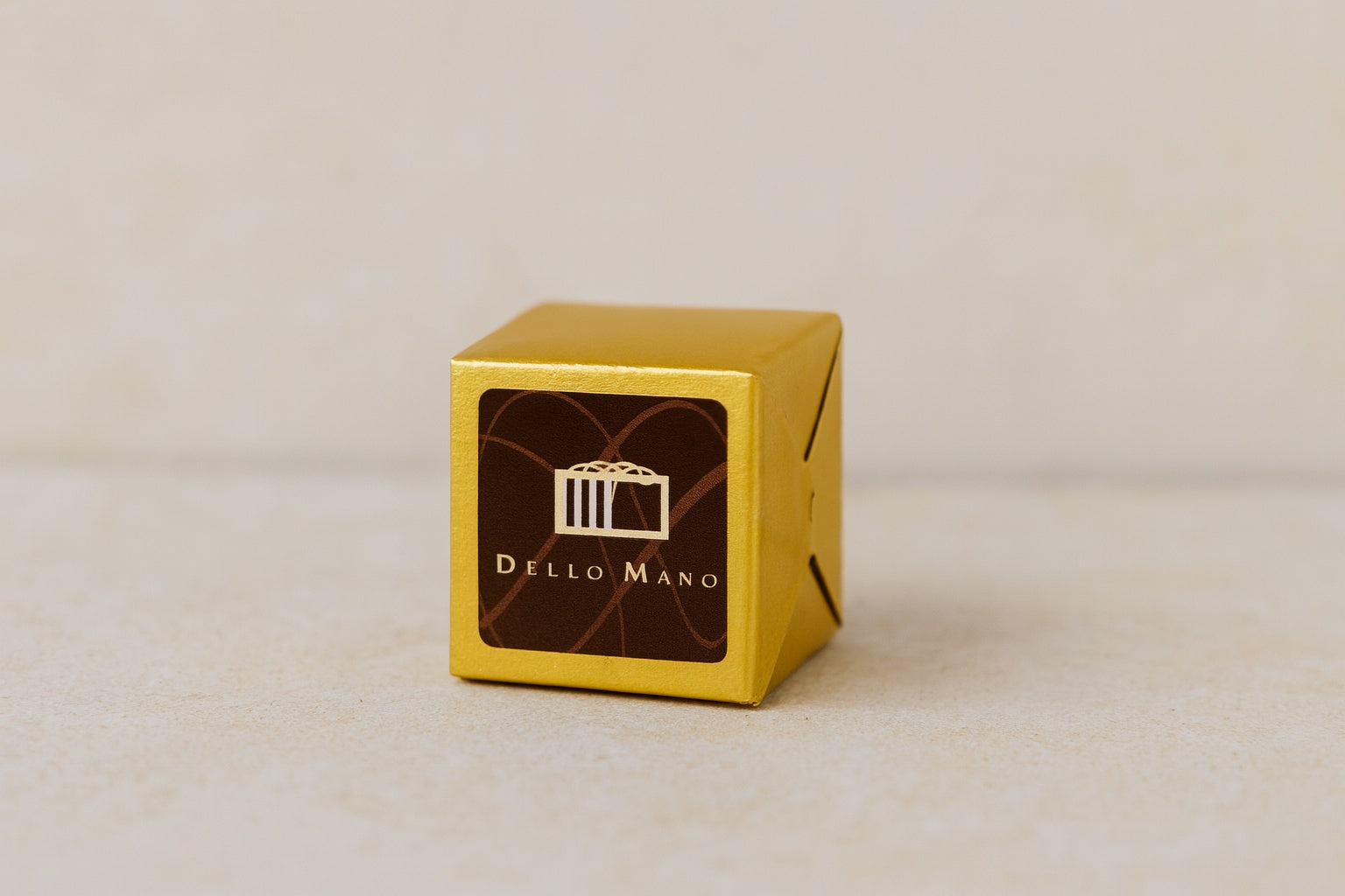 Classic Luxury Brownie Cube by Dello Mano, wrapped in gold foil with branded label, in a calm neutral setting, symbolising 18 years of handmade luxury
