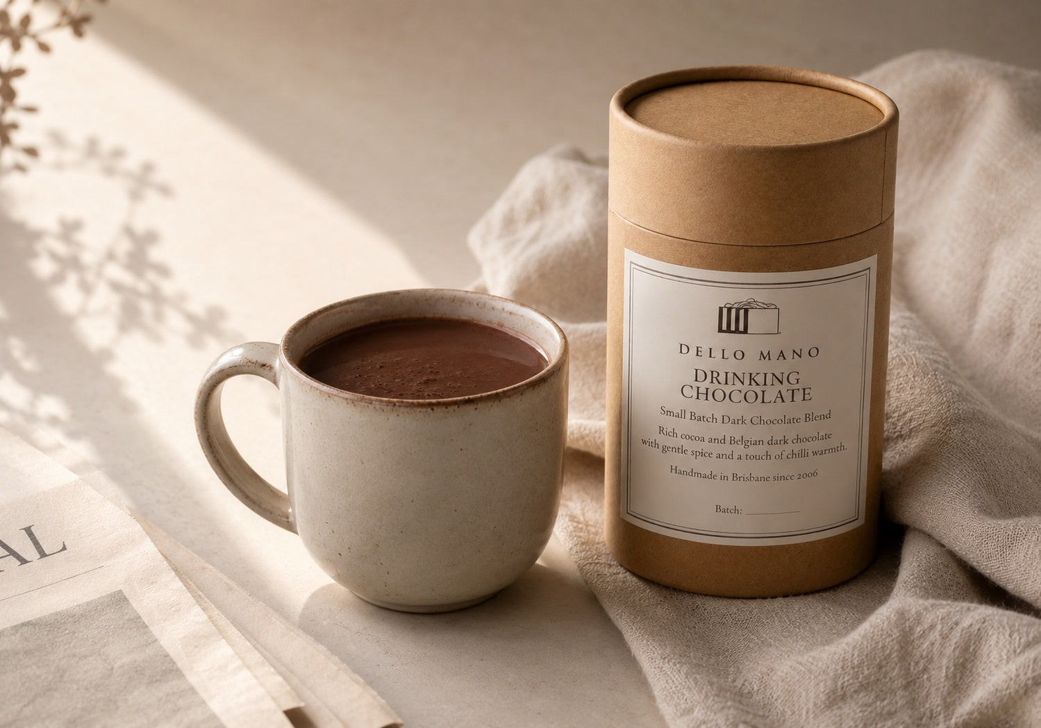 Dello Mano Dark Drinking Chocolate beside a ceramic mug of rich hot chocolate in soft morning light on neutral linen.