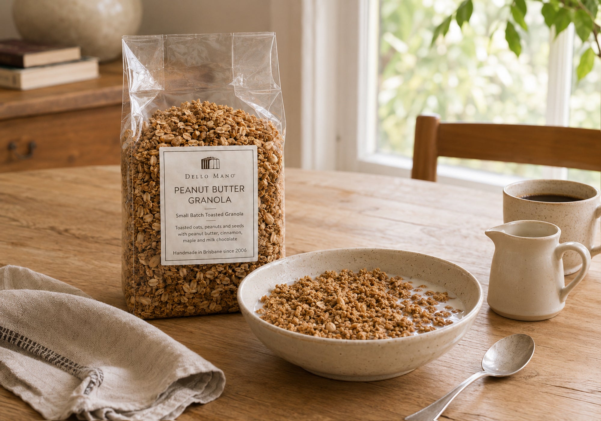 Dello Mano Peanut Butter Granola served with milk on a breakfast table beside the granola bag, coffee and a milk jug.