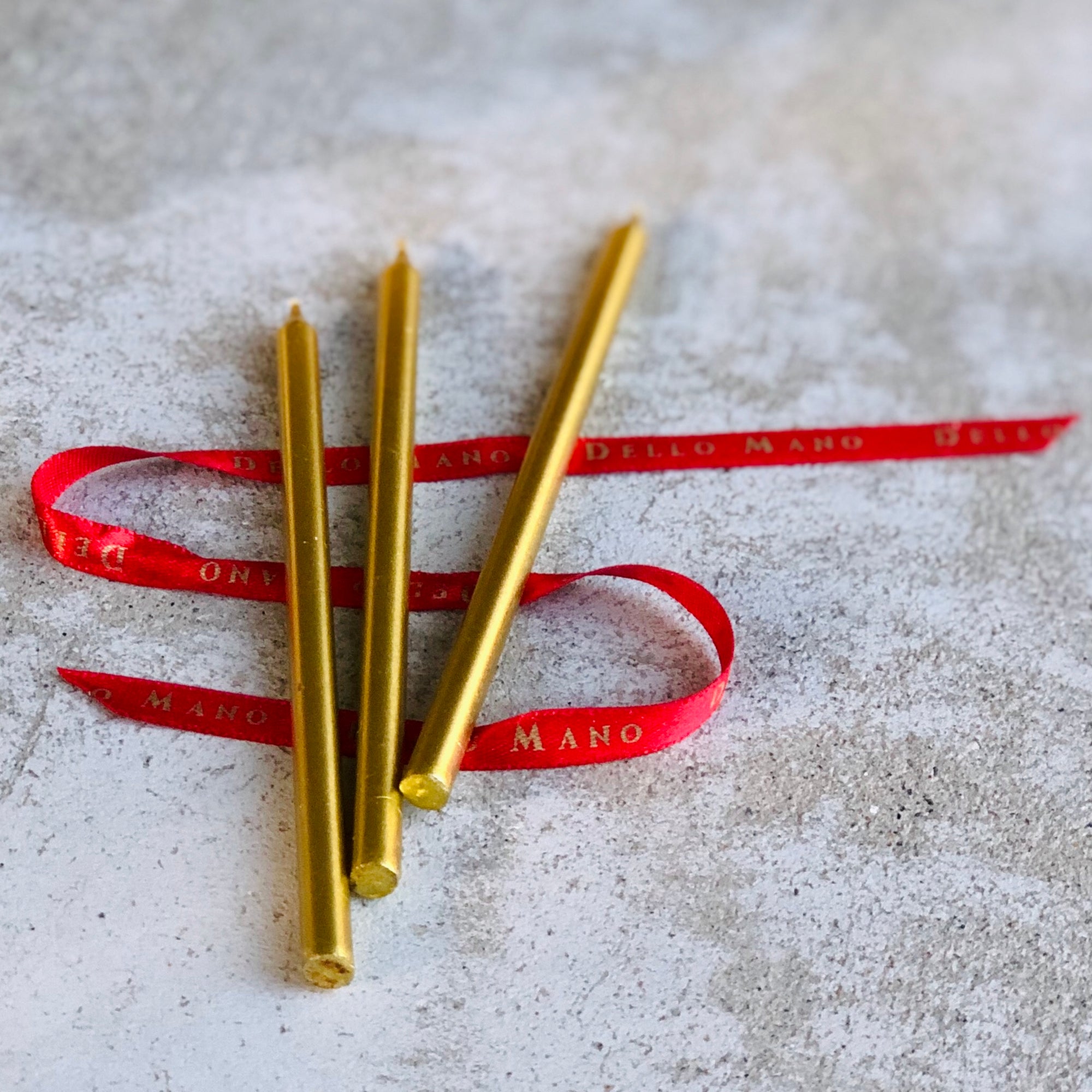 Dello Mano's signature gold candles resting on a red ribbon