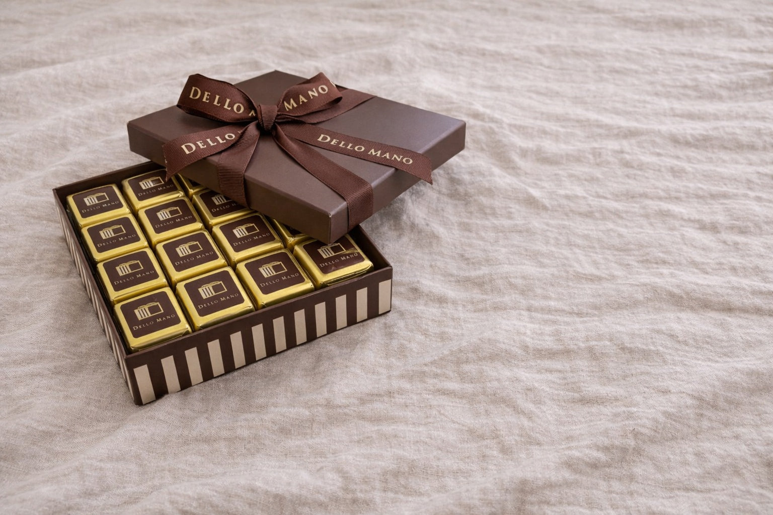 Open Dello Mano corporate brownie gift box on natural linen background with individually wrapped brownies ready to share