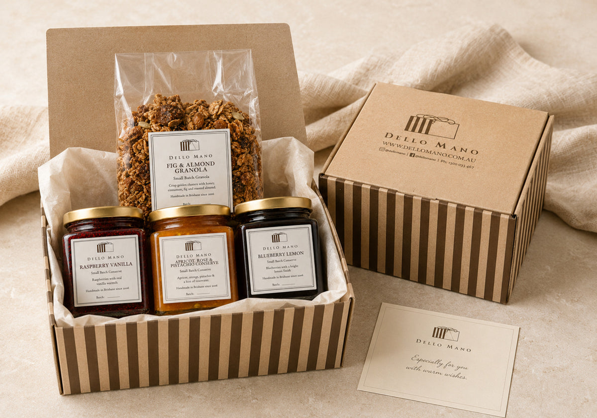 Gift-ready Dello Mano Breakfast Table Gift in a striped hamper with three fruit preserves, Fig & Almond Granola and a personal message card