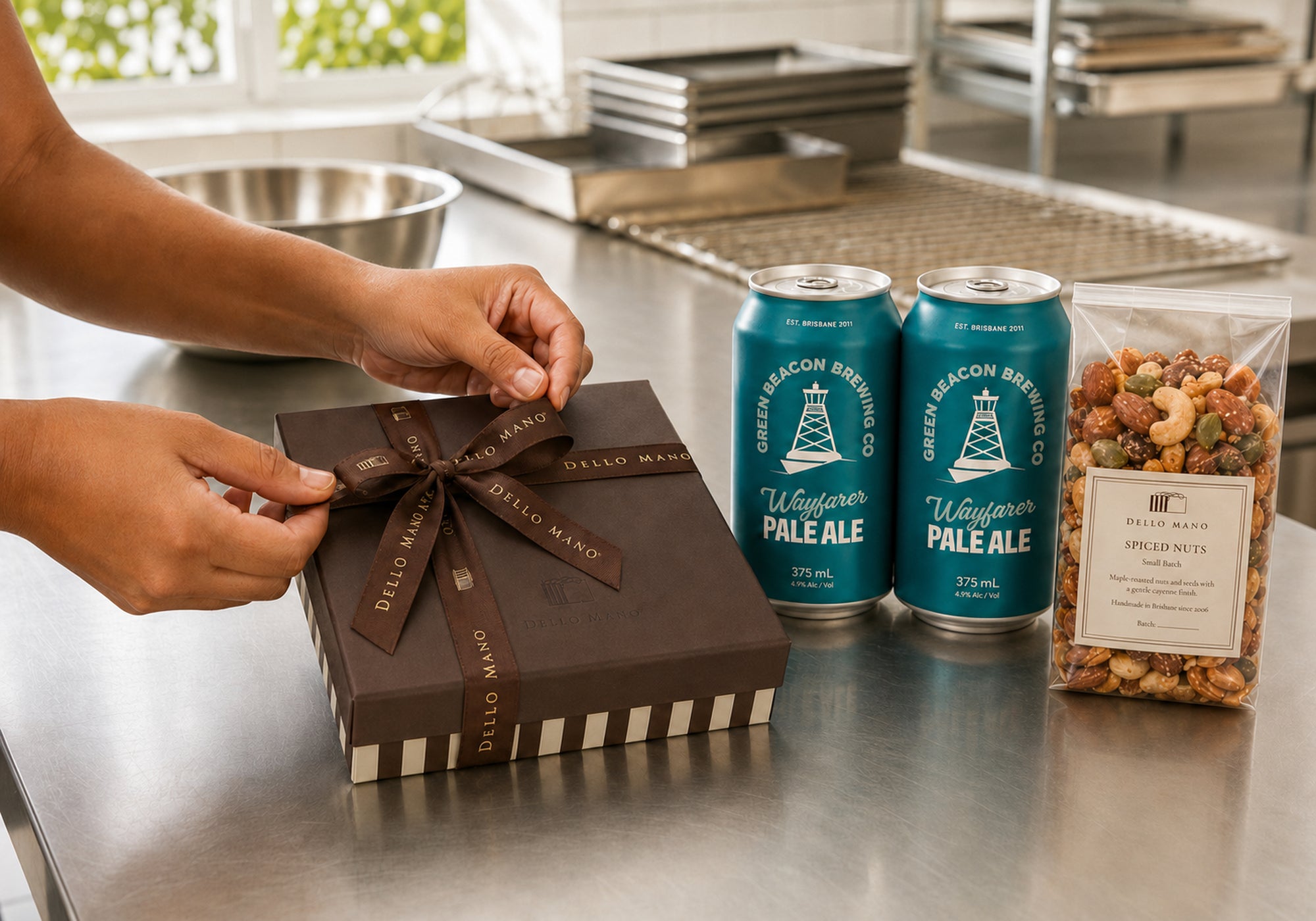 Dello Mano team member tying ribbon around a brownie gift box beside Brisbane-brewed Green Beacon Pale Ales and spiced nuts.