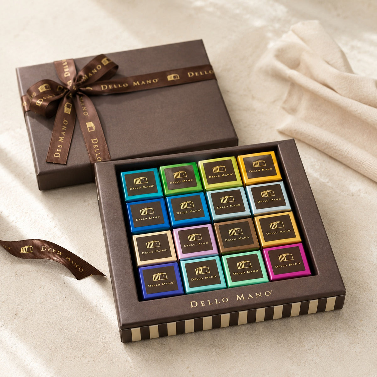 Open Dello Mano Signature Mixed Brownie Gift Box with colourful individually wrapped brownies on a warm neutral surface.