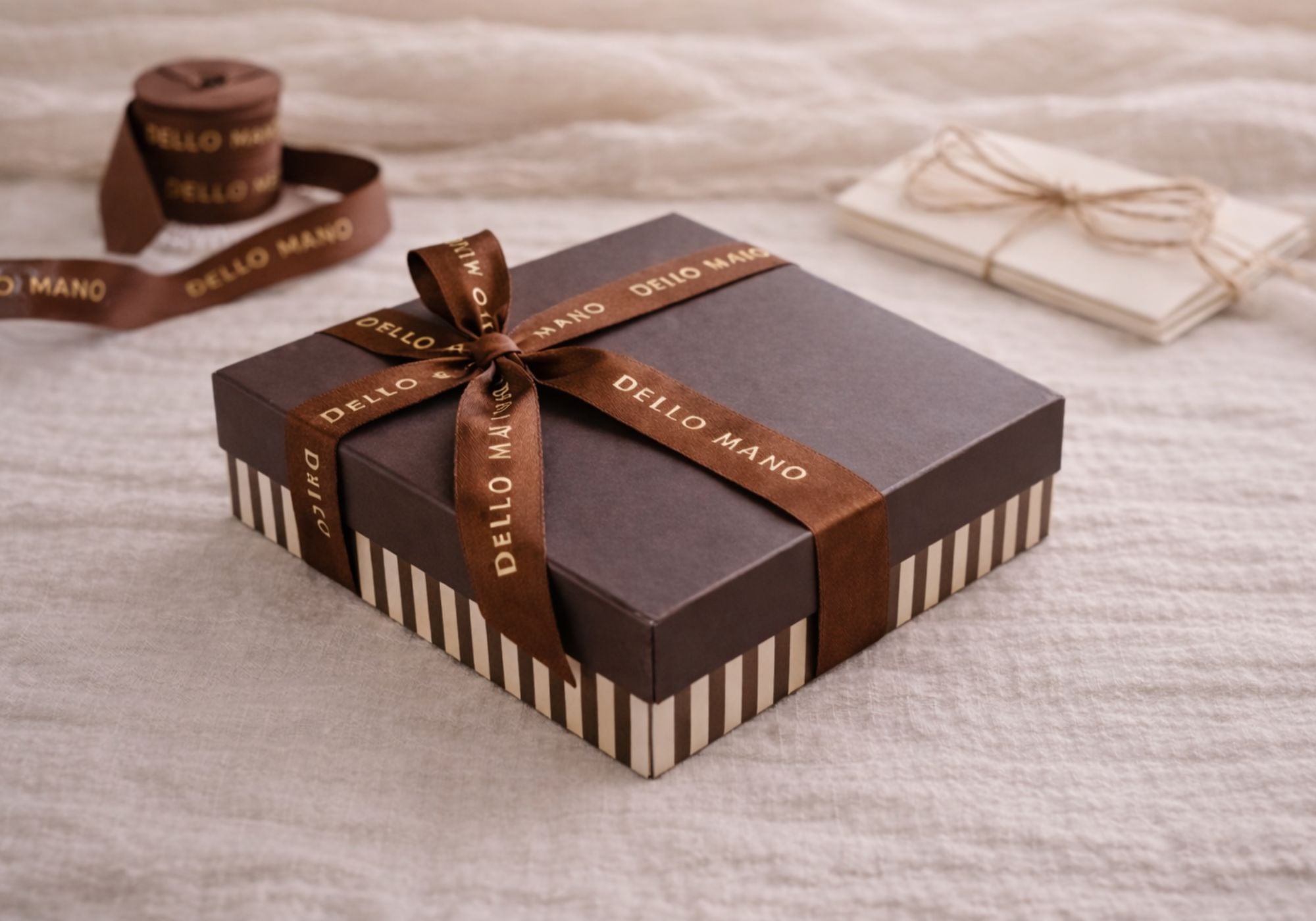 Dello Mano chocolate gift box wrapped with brown grosgrain ribbon beside gift cards on linen background