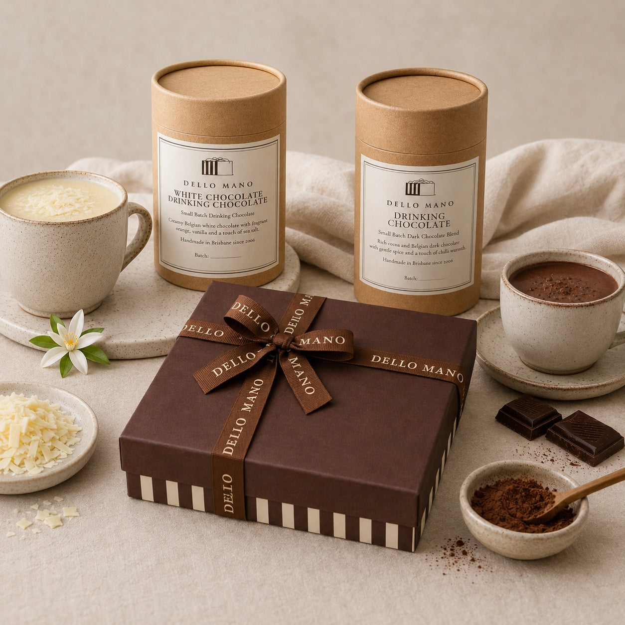 Dello Mano chocolate gifts with a branded brownie gift box, white and dark drinking chocolate, and cups of chocolate styled on soft neutral linen.