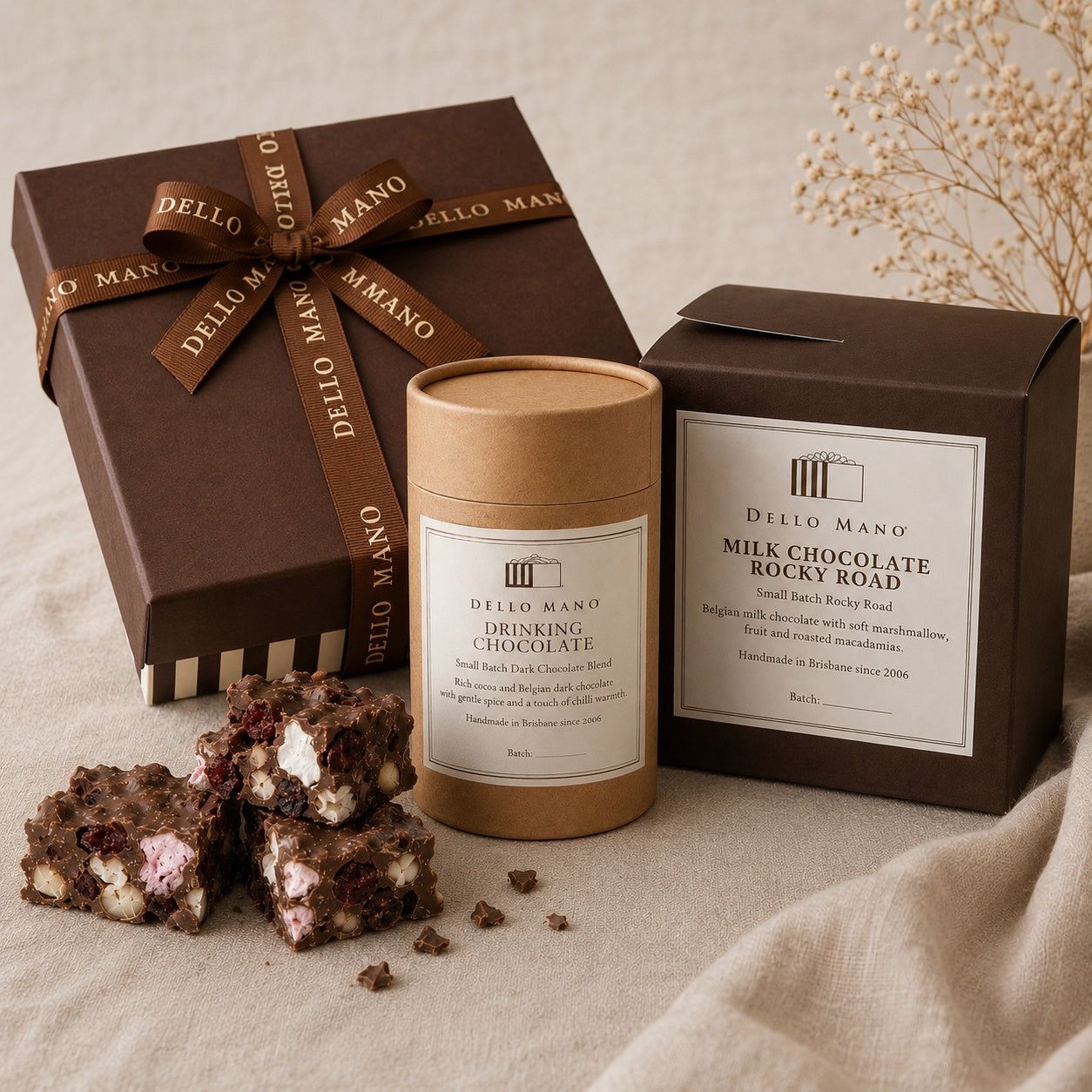 Dello Mano chocolate gift selection with a ribboned gift box, drinking chocolate and milk chocolate rocky road on soft neutral linen.