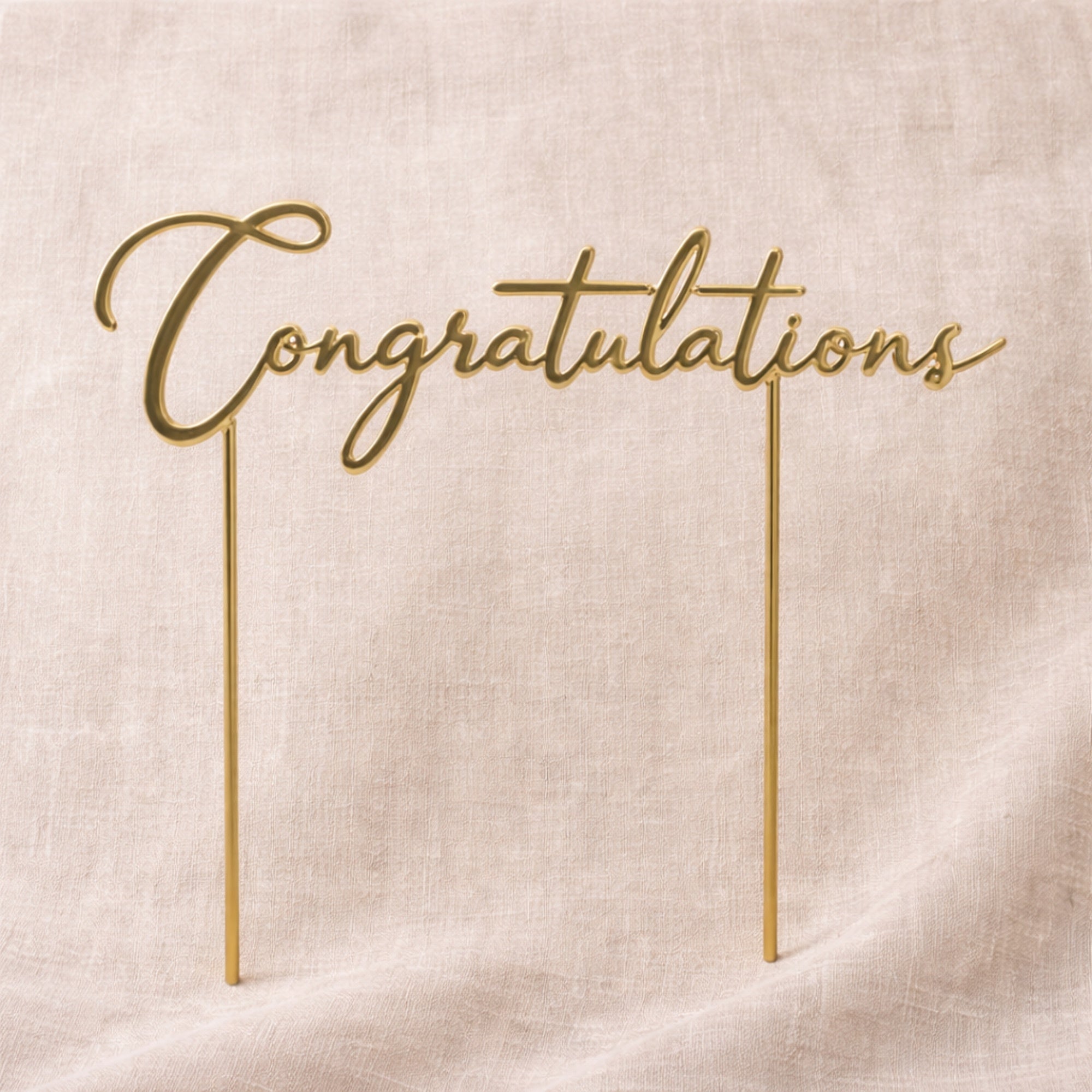 Gold "Congratulations" cake topper on neutral linen background – elegant cake decoration accessory