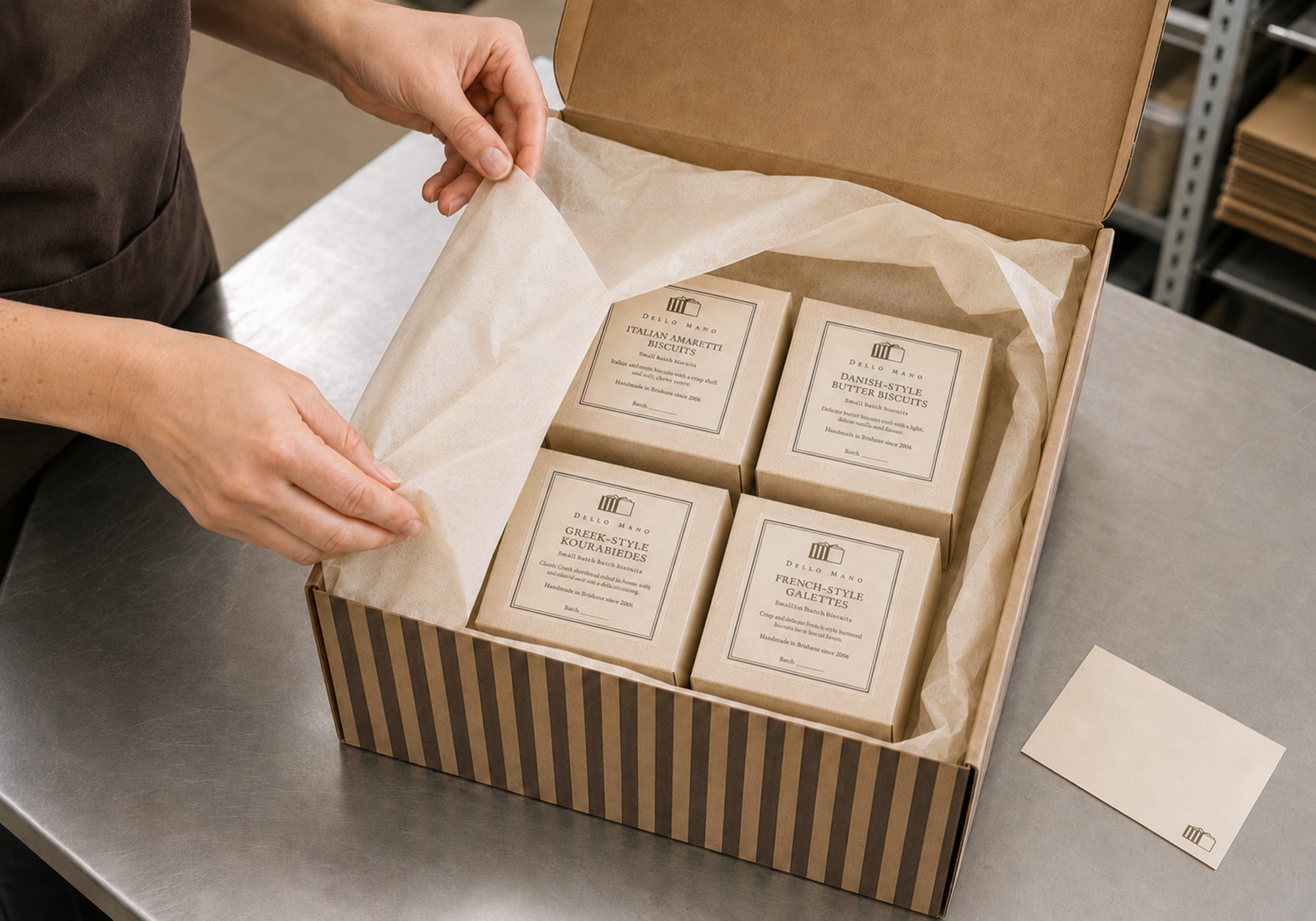 Dello Mano team member packing four European-inspired biscuit boxes with ivory tissue inside a striped gift hamper in Brisbane.